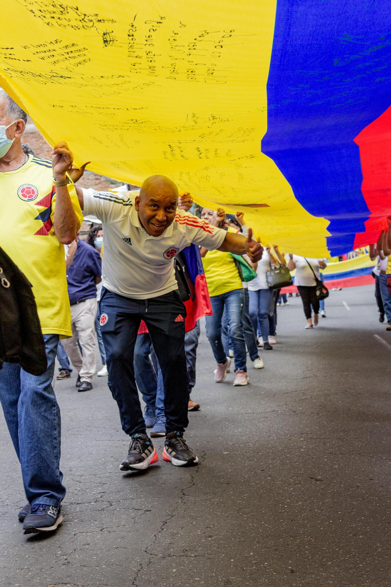 Participants in a Colombian demonstration hold a large national flag during a street event.