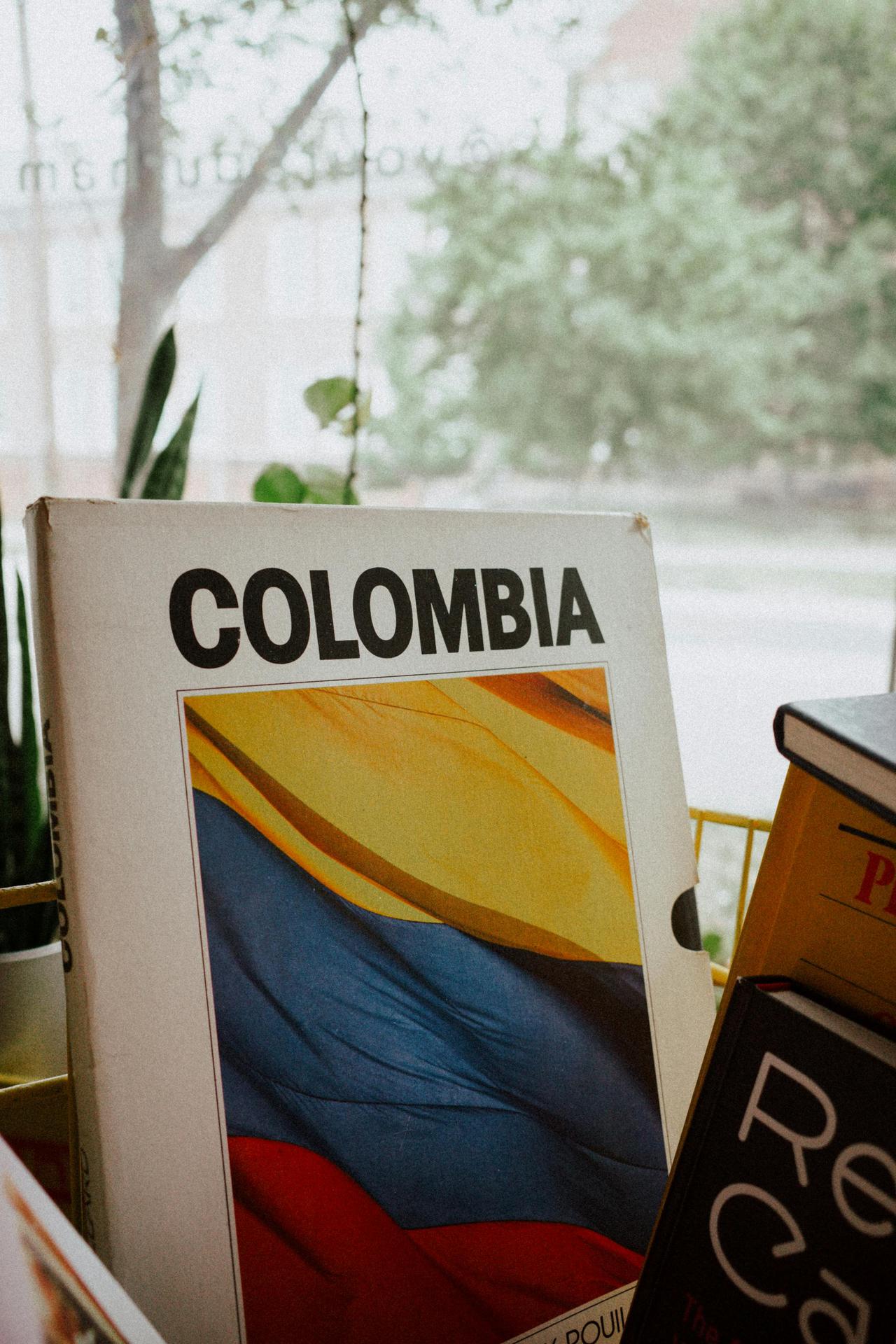 Vertical shot of a book with the Colombian flag displayed on its cover, indoors by a window.
