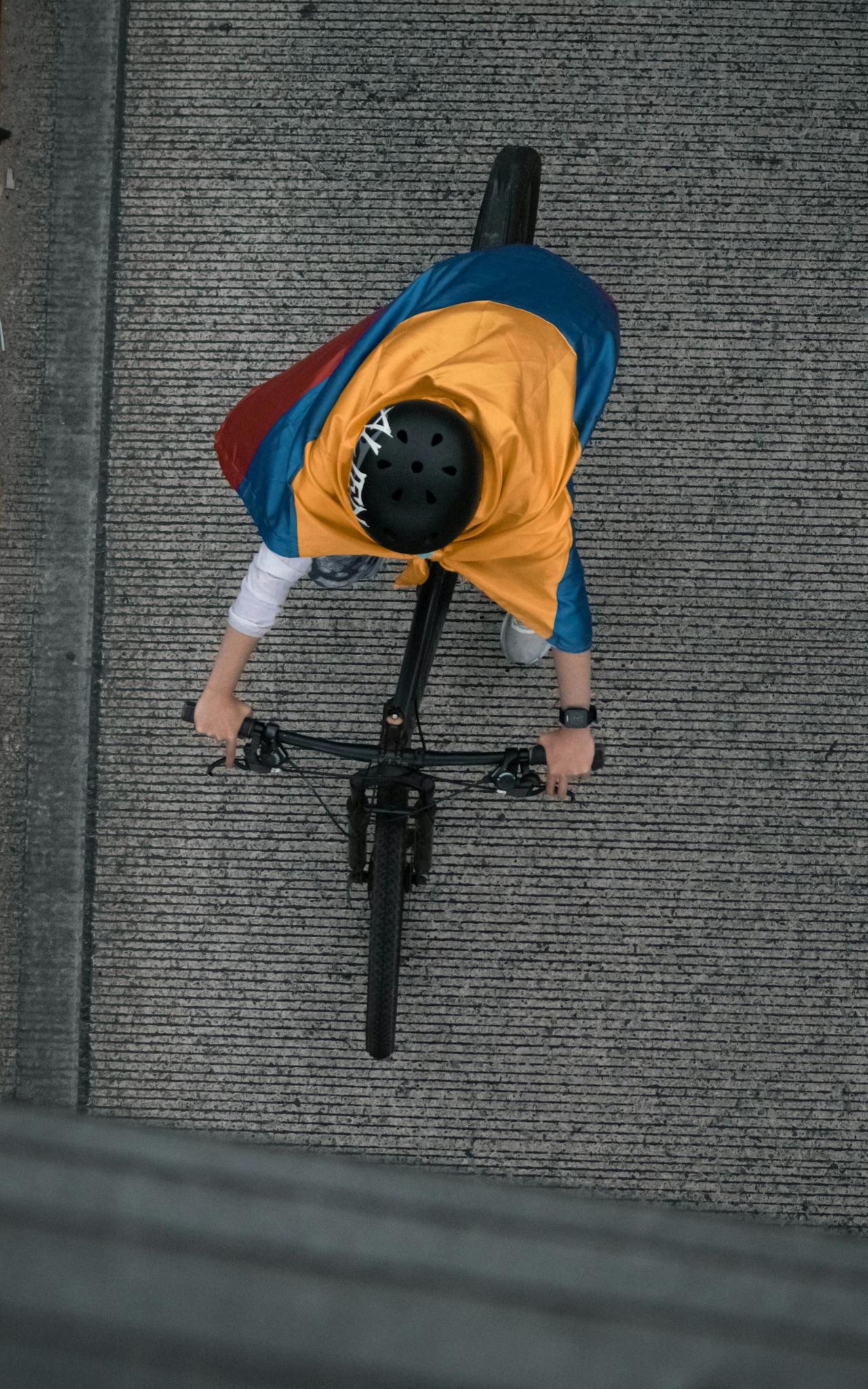 A child wearing a Colombian flag cape rides a bicycle, viewed from above.