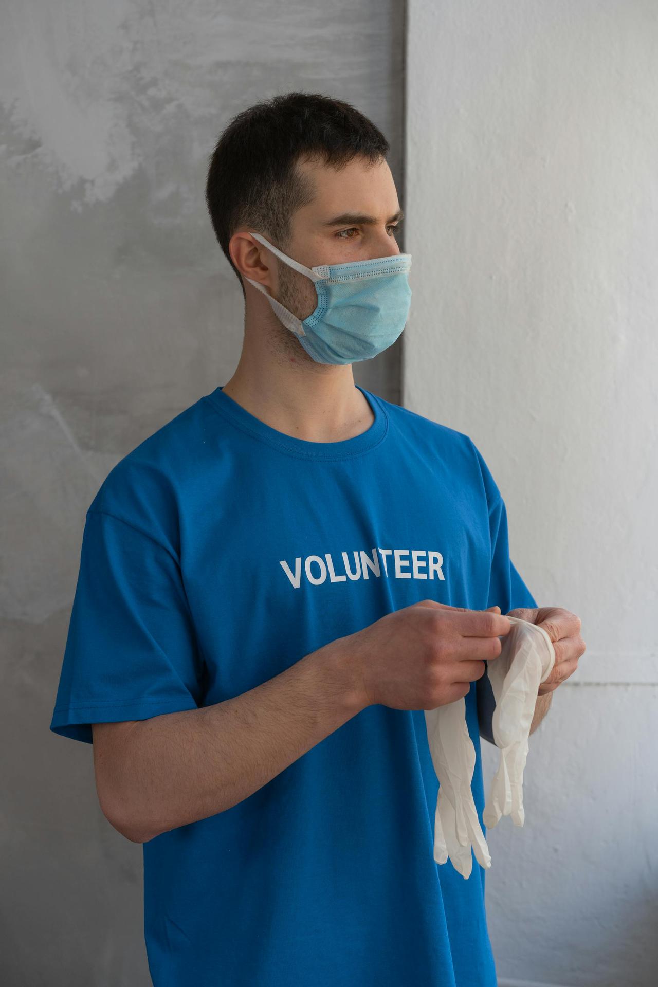 A volunteer wearing a face mask prepares for community service with surgical gloves.