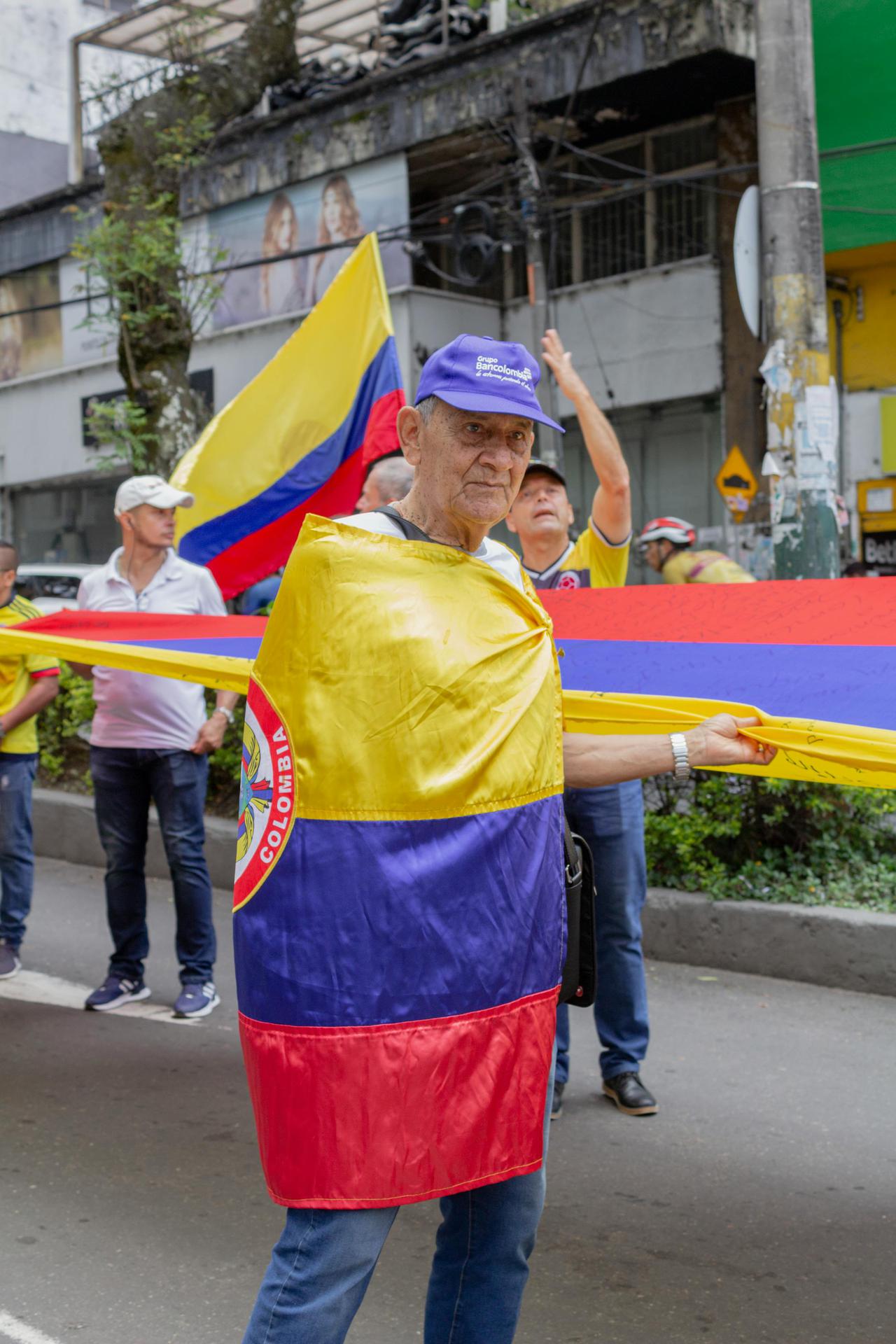 Elderly man wrapped in Colombian flag participating in outdoor celebration in Ibagué, Colombia.