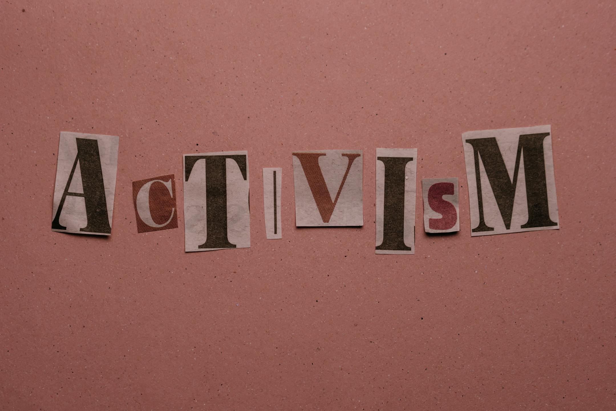Paper cutouts spelling 'Activism' on a pink surface, emphasizing social movement themes.