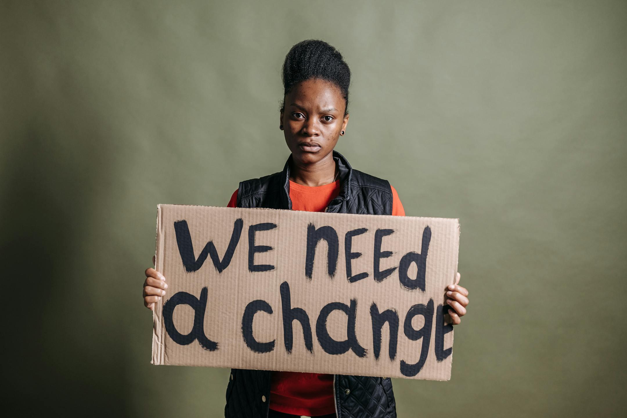 Portrait of an activist with a placard stating 'We need a change', highlighting human rights.