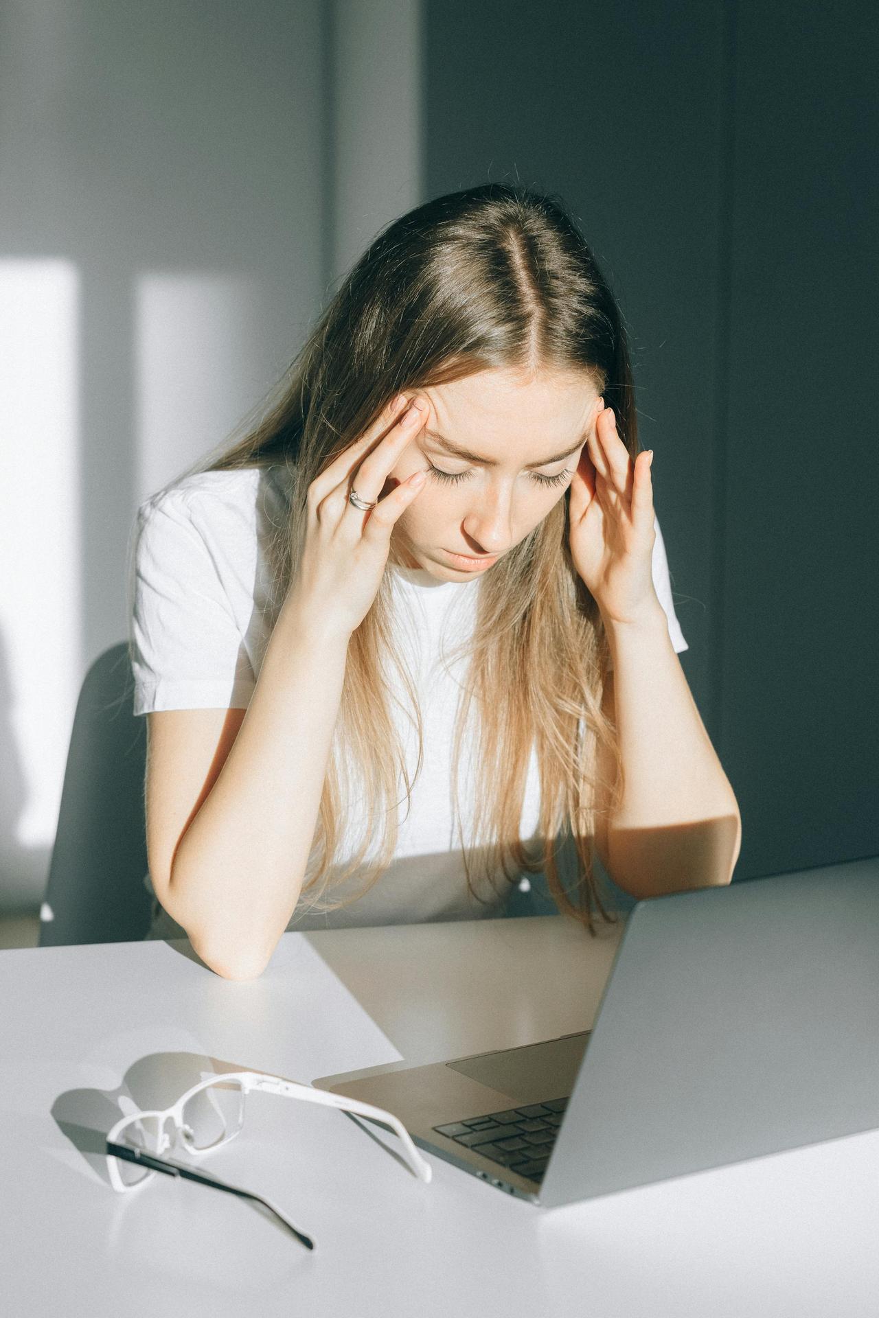 Stressed young woman with a headache working on a laptop indoors.