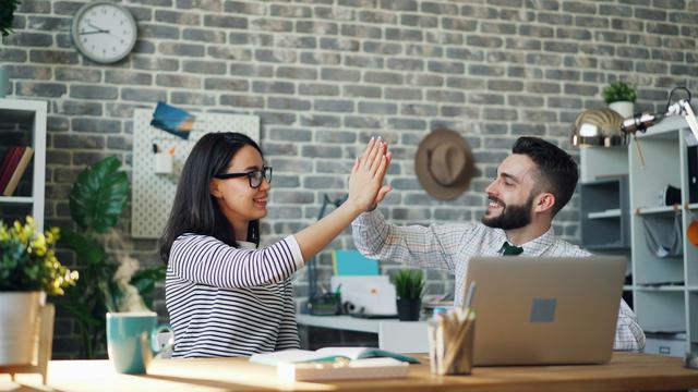 happy coworkers doing high-five in office at desk with laptop