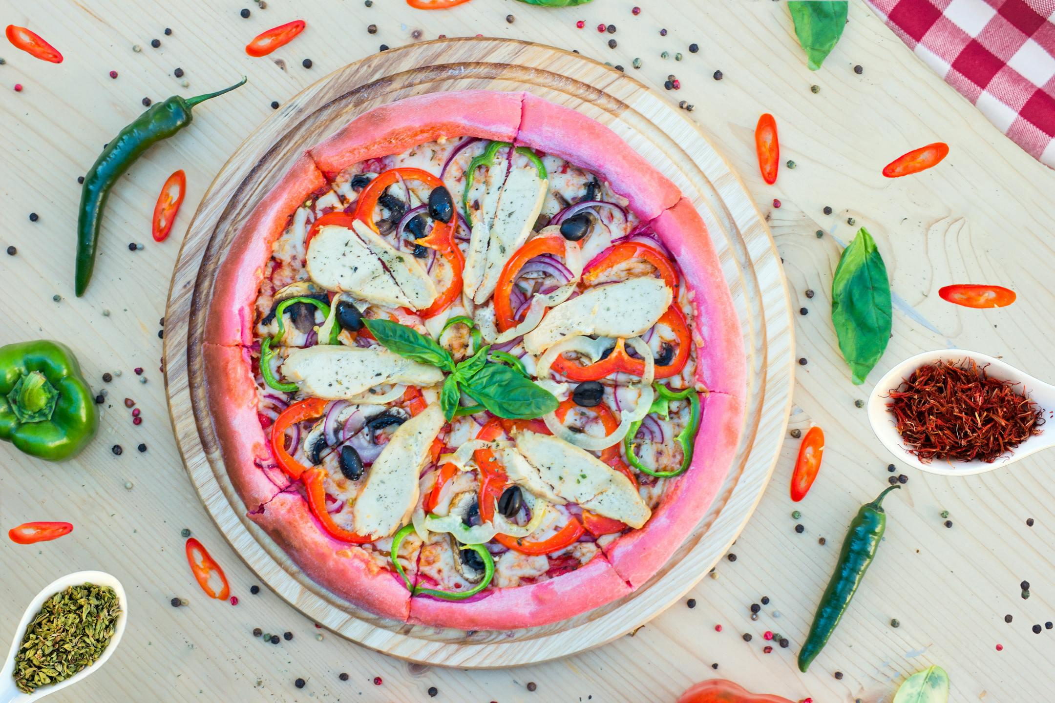 Colorful pink crust pizza with vegetables and herbs on a wooden platter. Perfect for food lovers.