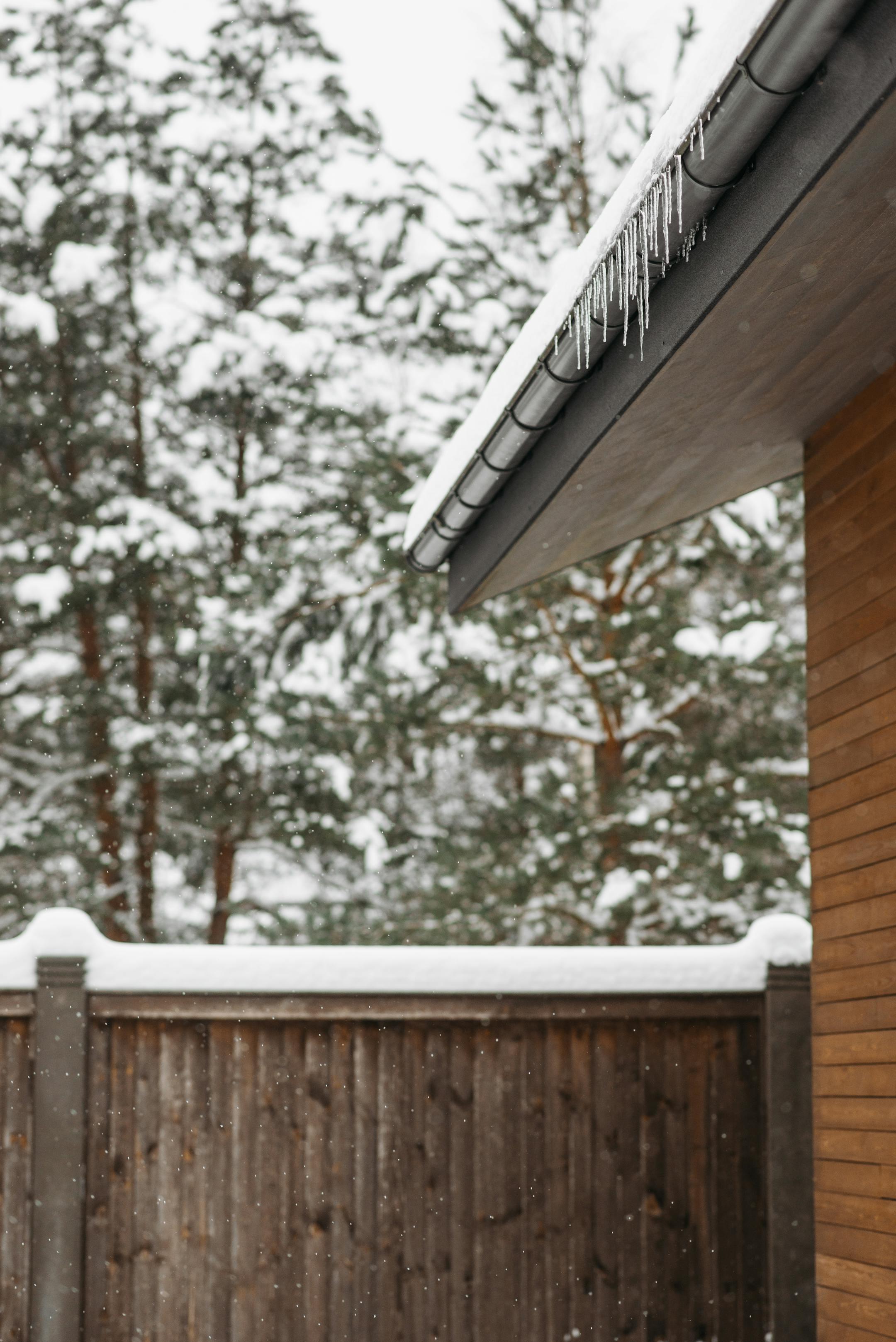 Snow-covered roof with icicles and a wooden fence in a winter landscape.