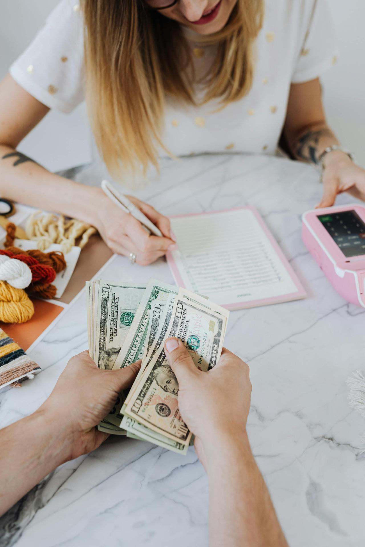 Two adults organizing finances with cash, planner, and card machine indoors.