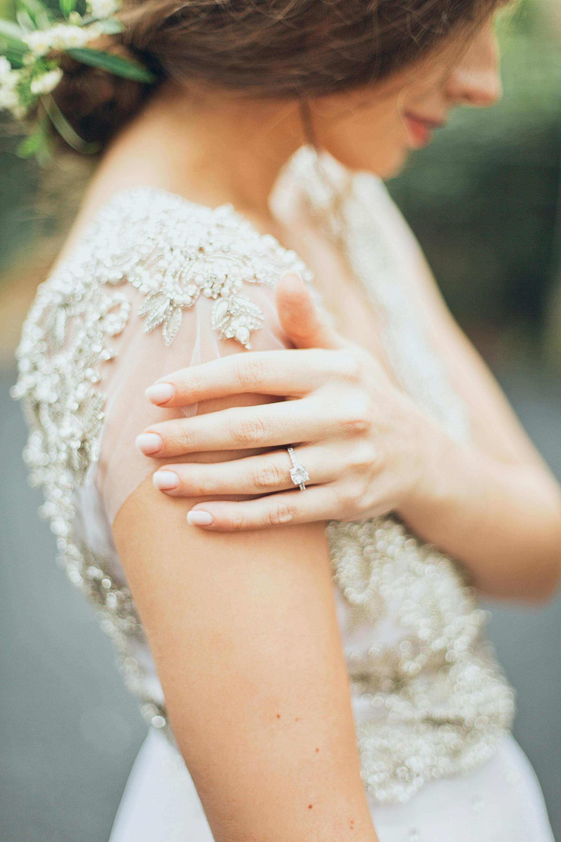 Close-up of a bride showcasing a wedding ring and intricate gown details outdoors.