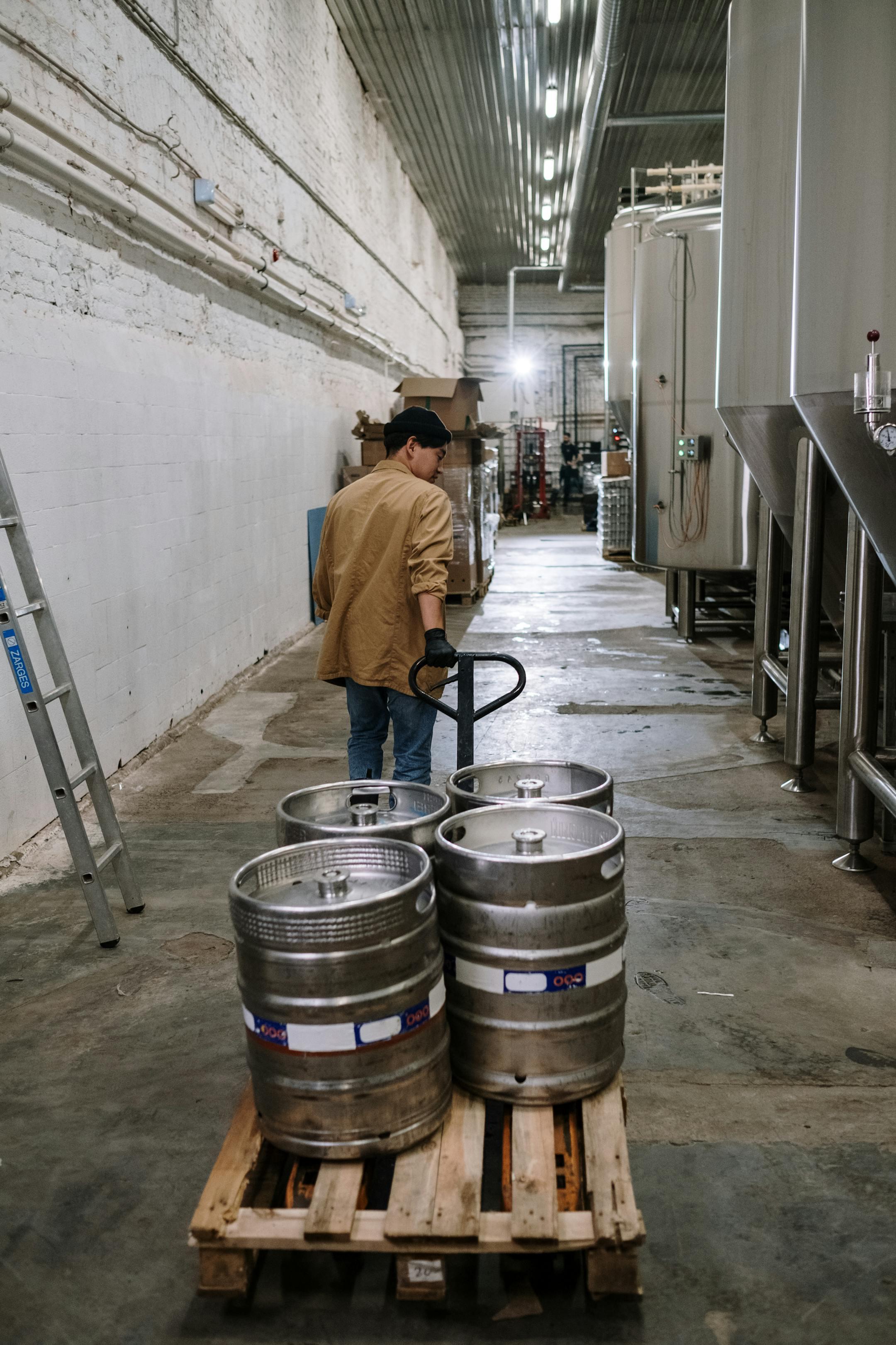 A worker in a brewery transports beer barrels on a pallet, showcasing the industrial beer-making process.