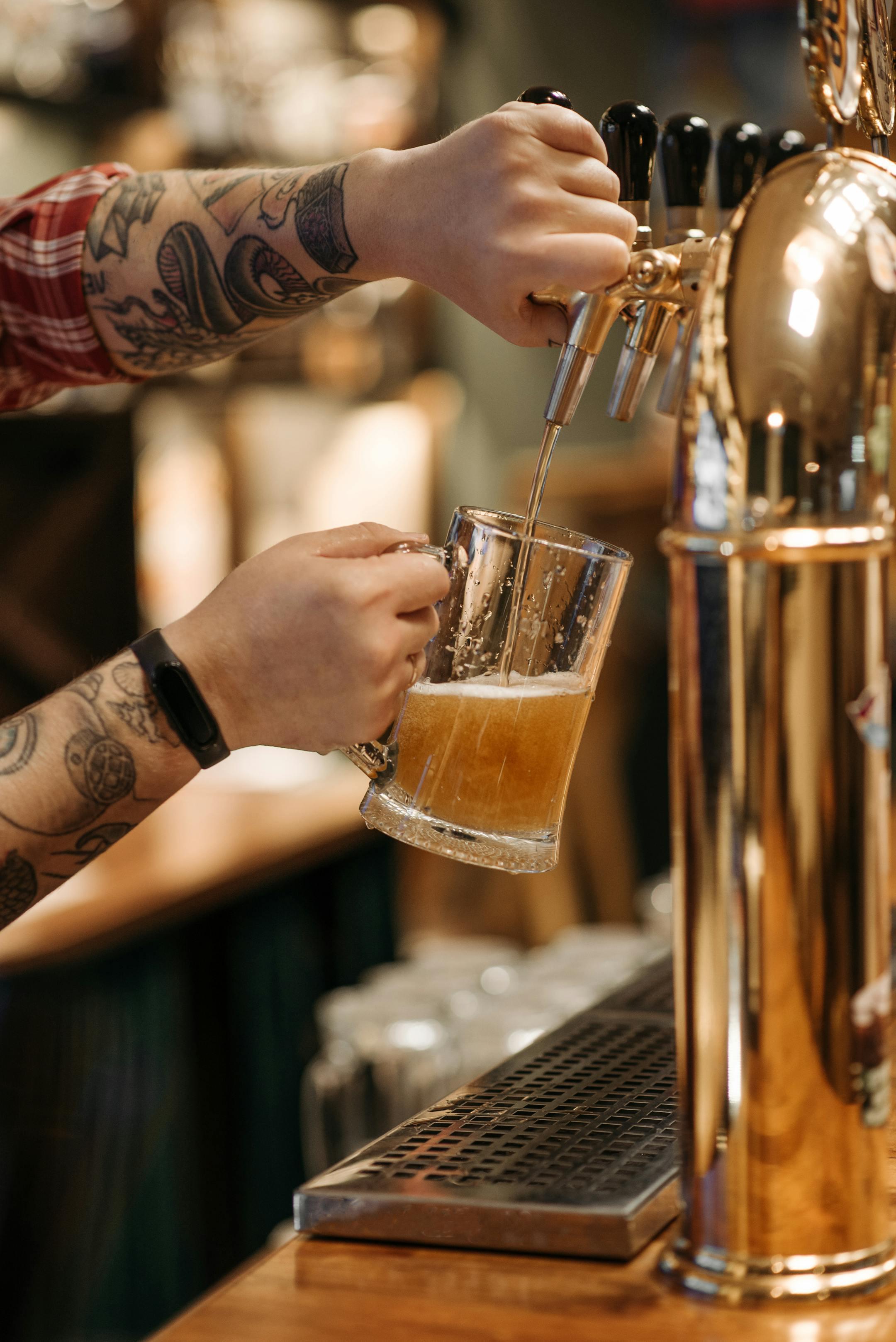 Close-up of a tattooed bartender pouring craft beer into a glass.