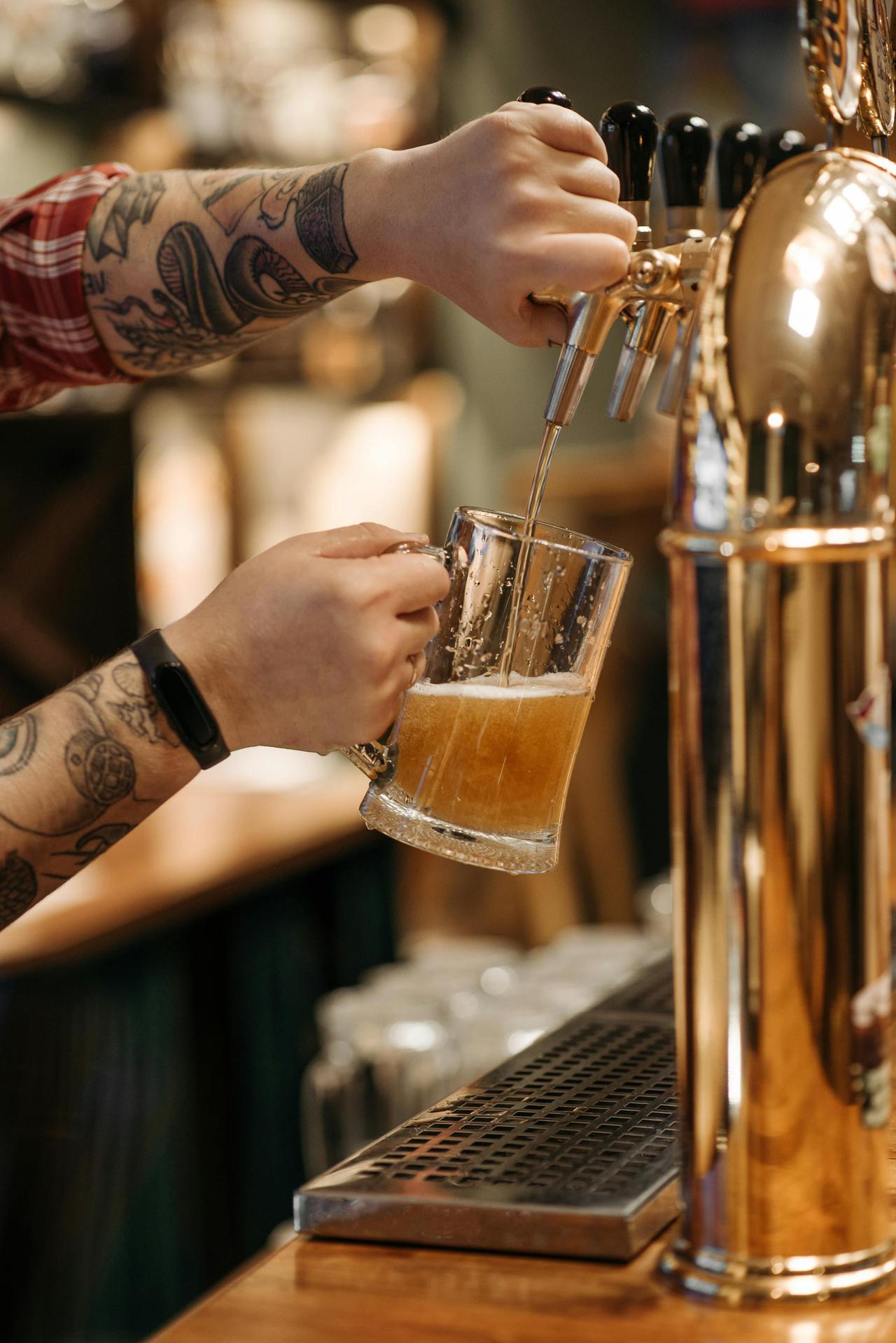 Close-up of a tattooed bartender pouring craft beer into a glass.