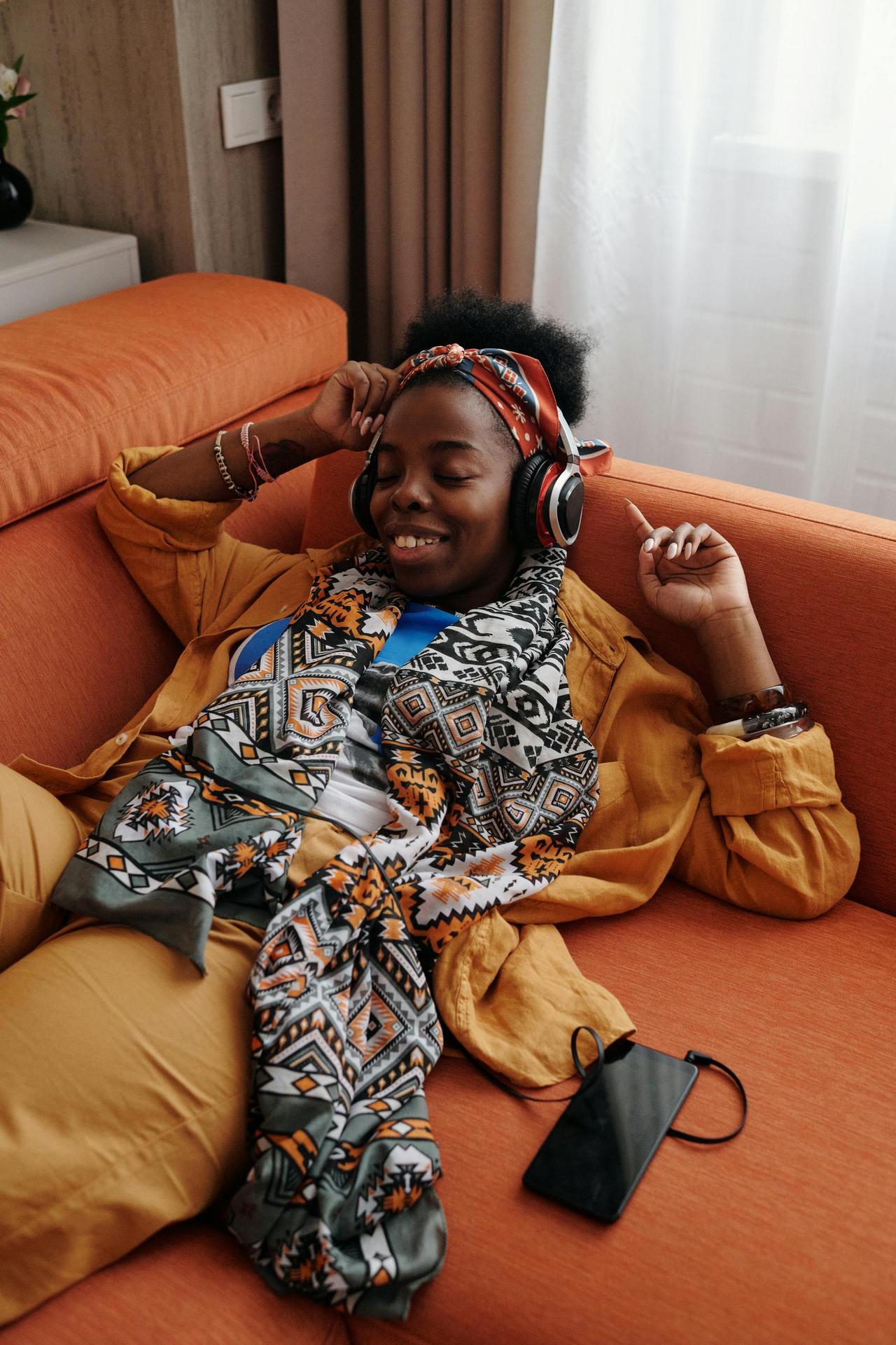 Smiling woman in headphones relaxing on a sofa, enjoying music indoors.