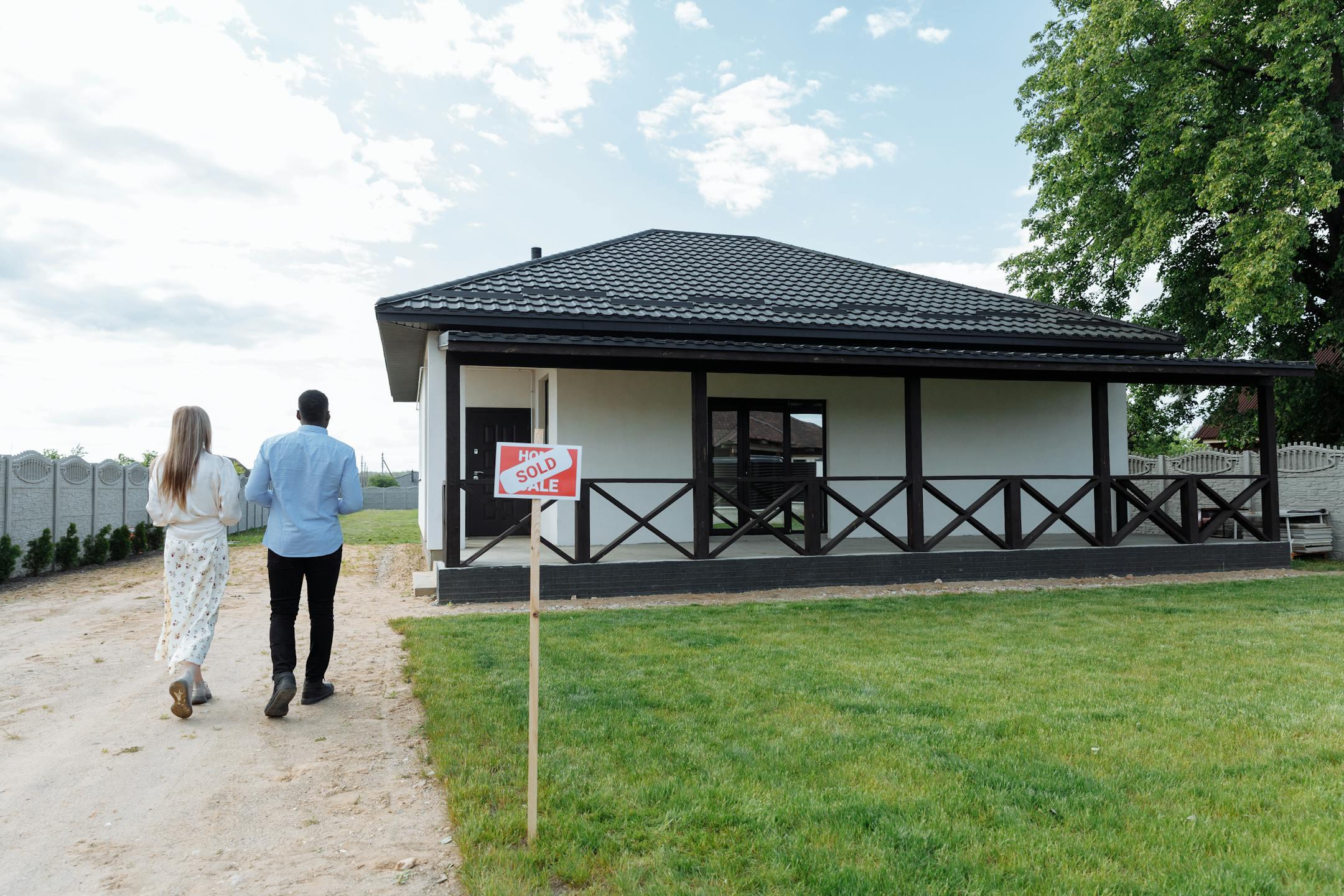 A couple walks towards their newly purchased home; a sign indicates the house is sold.