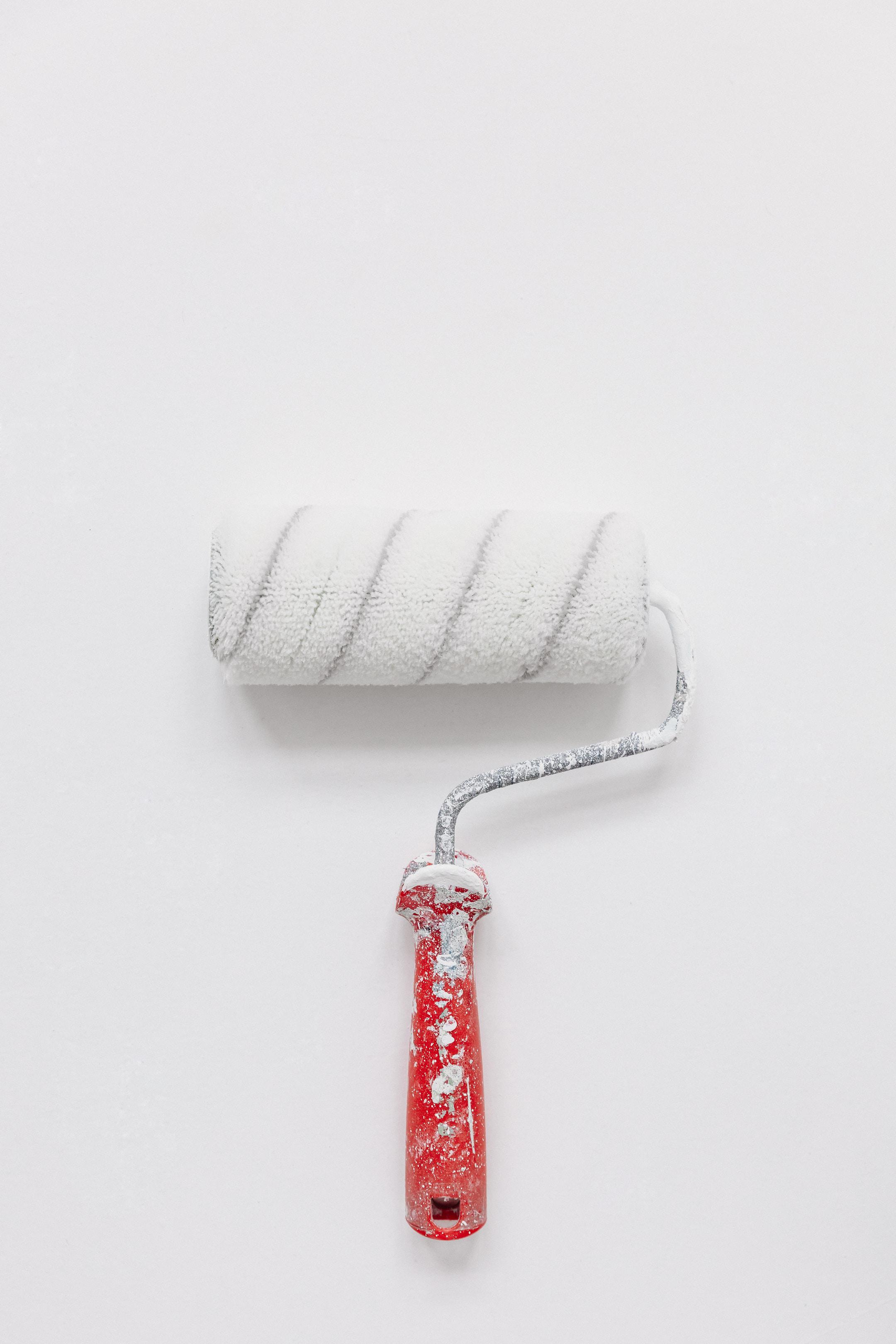 A paint roller painting a wall white.