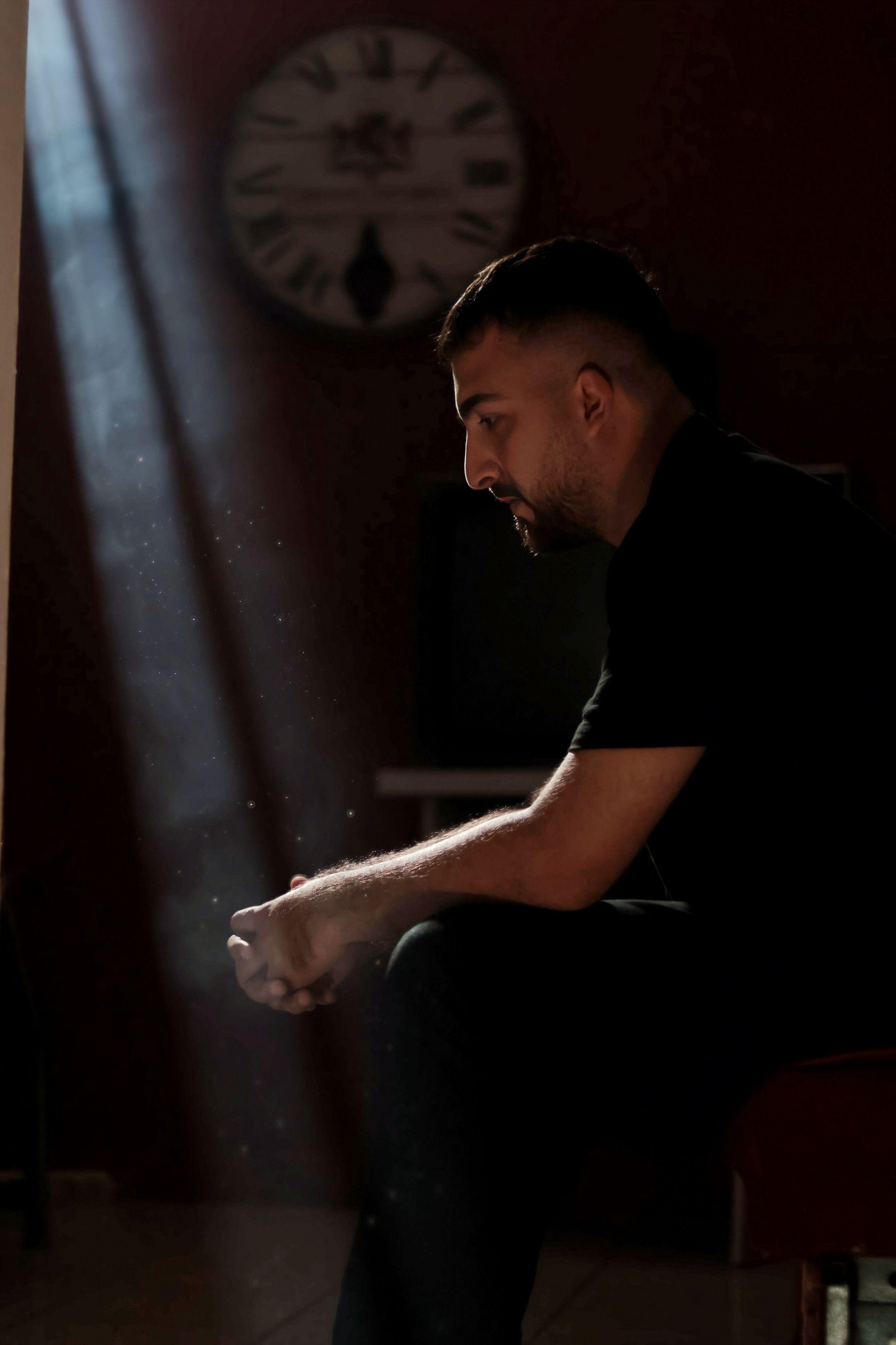 A man sitting thoughtfully in a dimly lit room with a beam of light highlighting dust particles