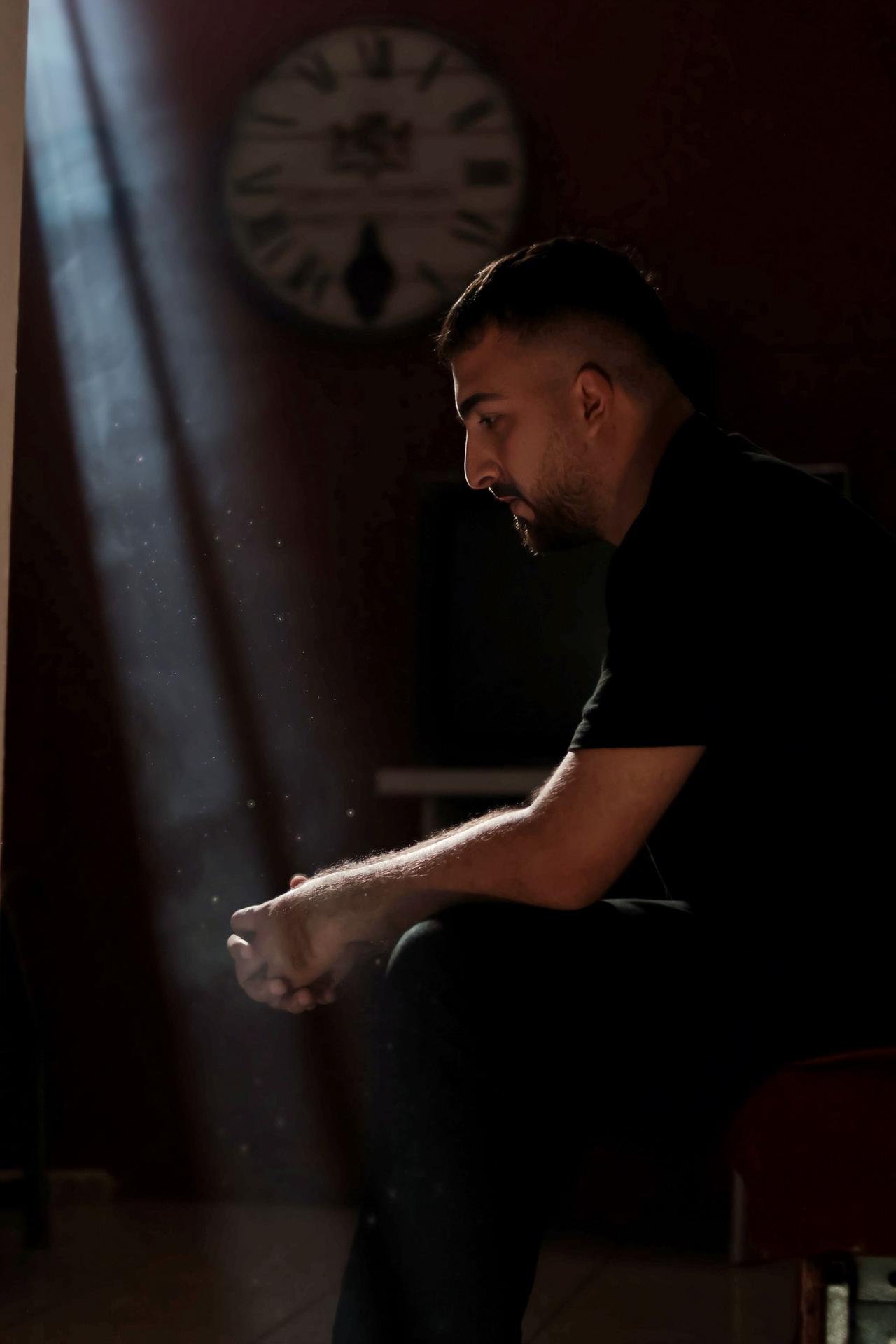 A man sitting thoughtfully in a dimly lit room with a beam of light highlighting dust particles