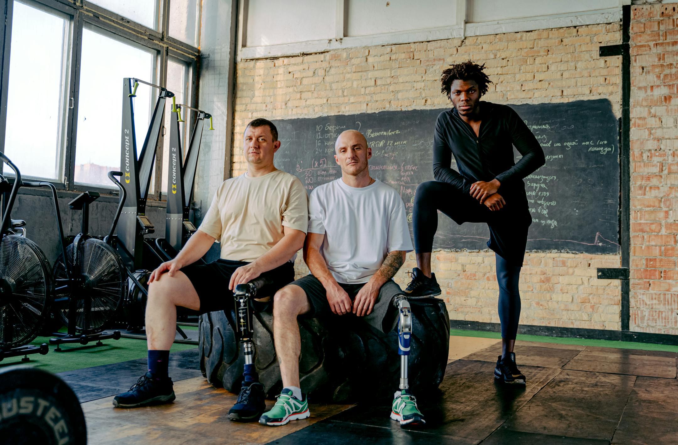 Diverse group of men with prosthetic legs posing confidently in a gym setting, showcasing strength and inclusivity.