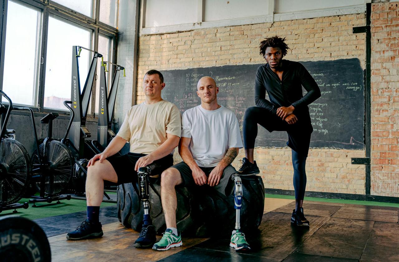 Diverse group of men with prosthetic legs posing confidently in a gym setting, showcasing strength and inclusivity.