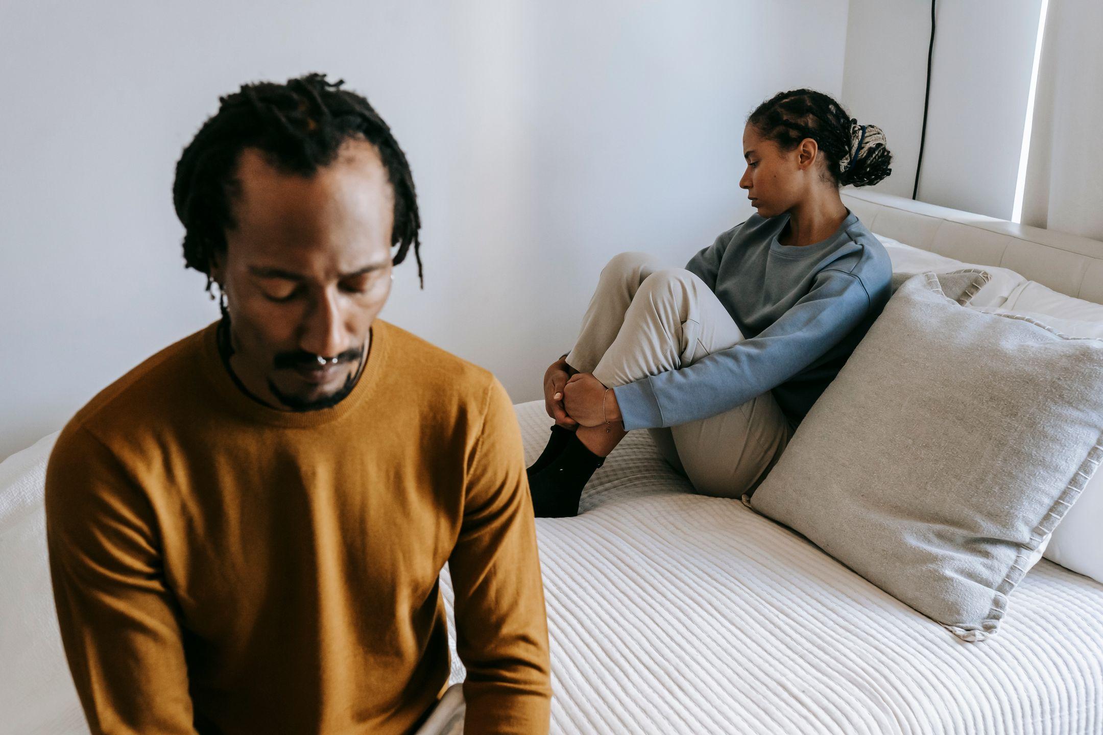 Young black couple in casual outfit spending time on bed with sad face in daytime at home