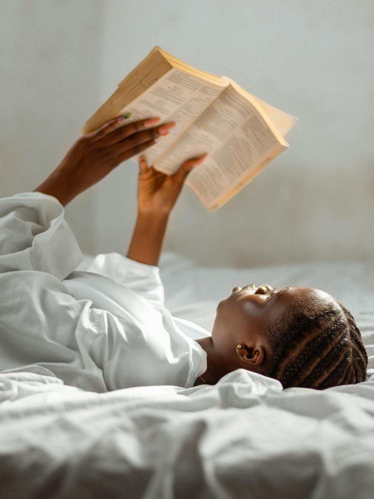 A woman lies comfortably on a bed, absorbed in reading a book, conveying peaceful solitude.