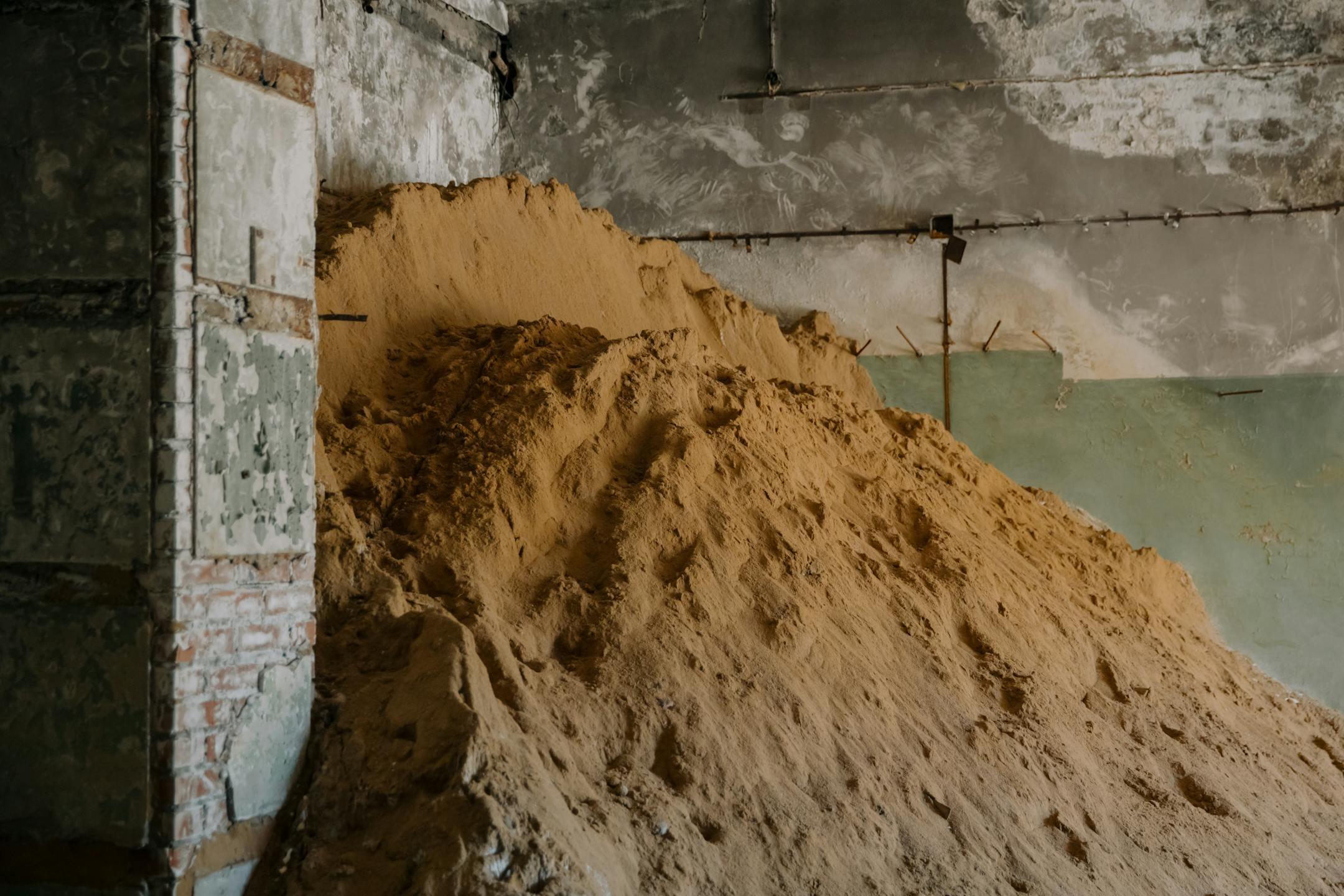 A large pile of sand inside an aged industrial building, showcasing urban decay.