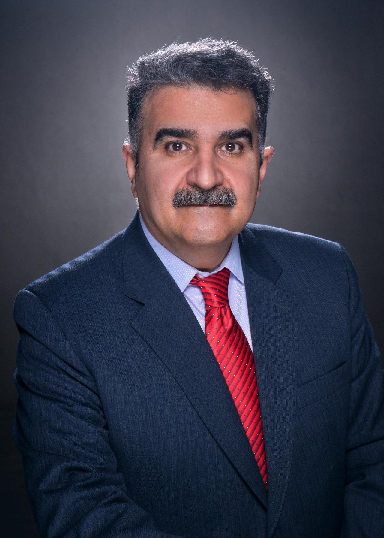 Portrait of a middle-aged man with a mustache in a blue suit and red tie, studio shot.