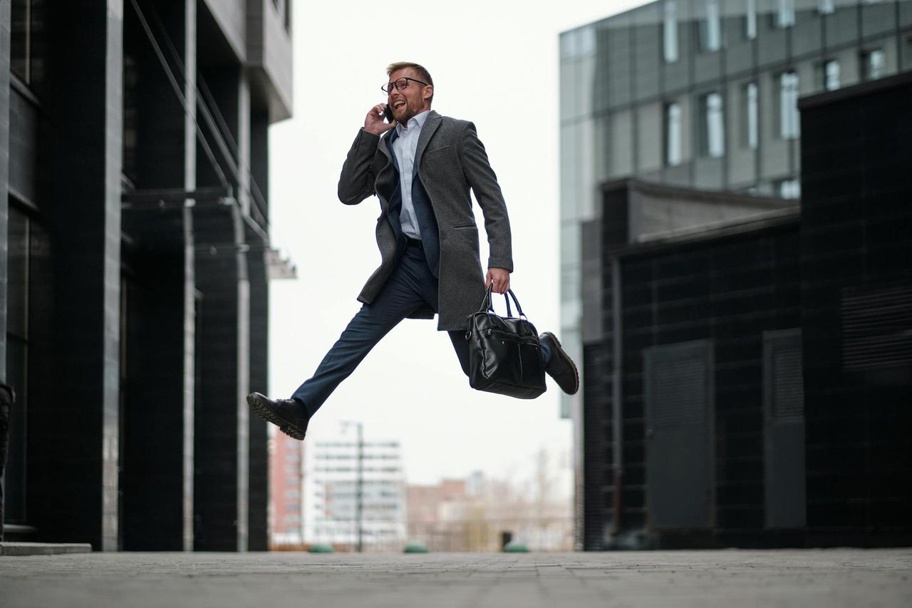 Dynamic businessman jumping while talking on phone in a modern cityscape.