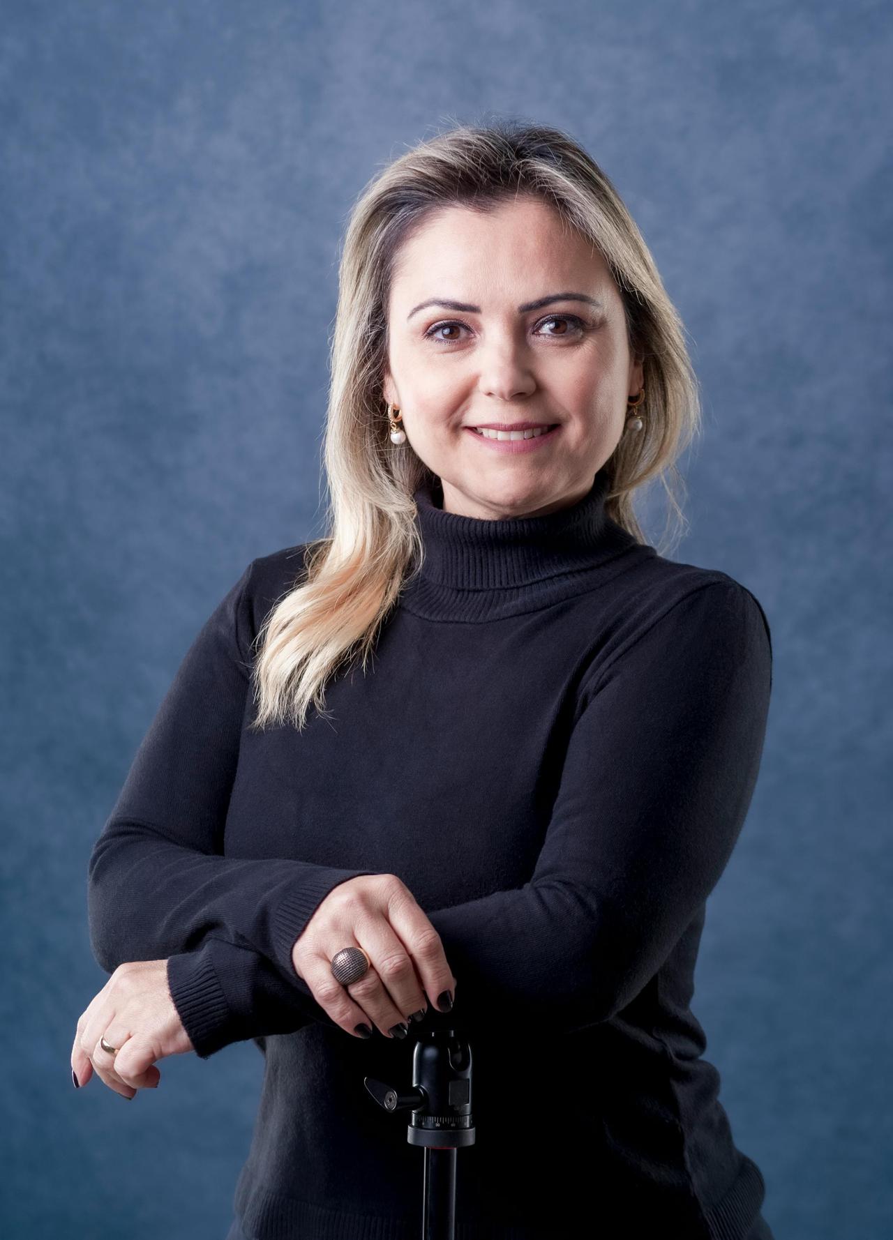 Studio portrait of a middle-aged woman in a black sweater against a blue background.