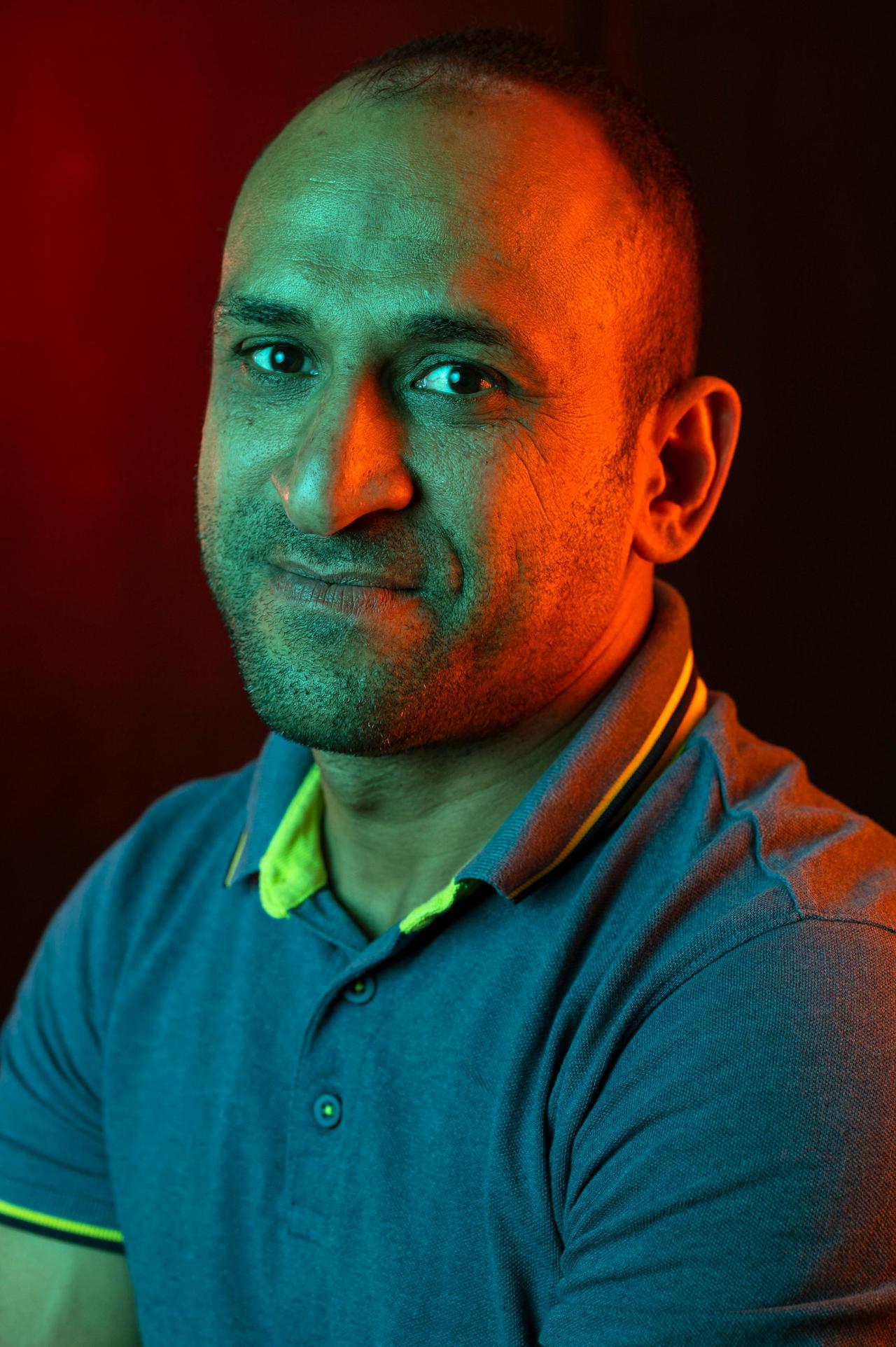 A portrait of a bald man with facial hair in a polo shirt, lit with vibrant studio lighting.
