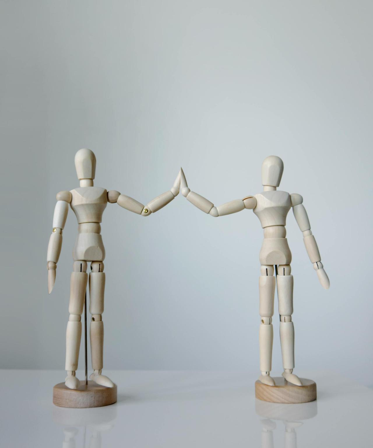 Two wooden artist mannequins engaged in a high-five, representing teamwork and cooperation.