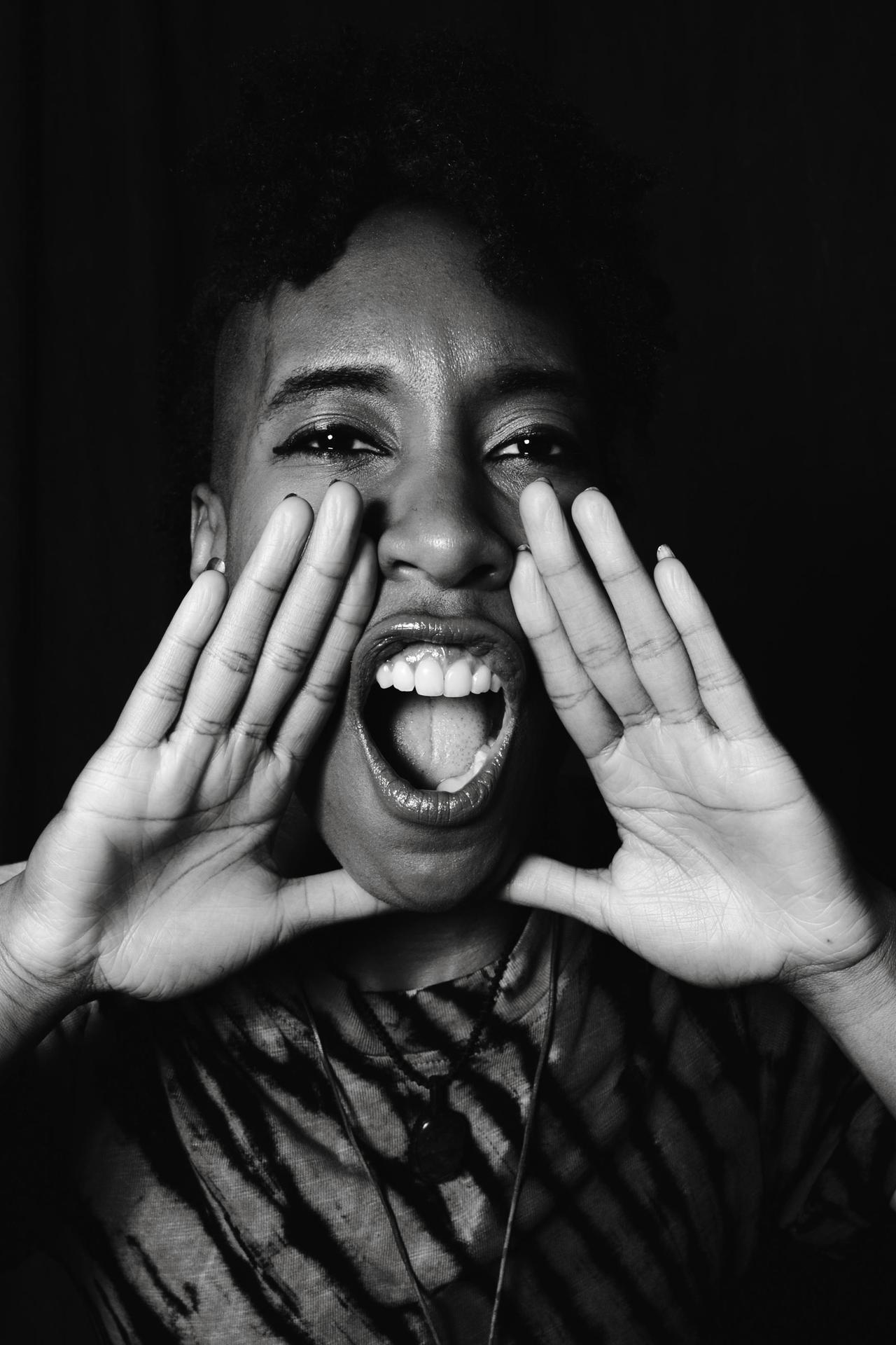 Grayscale portrait of a black woman energetically shouting, conveying strong emotions.