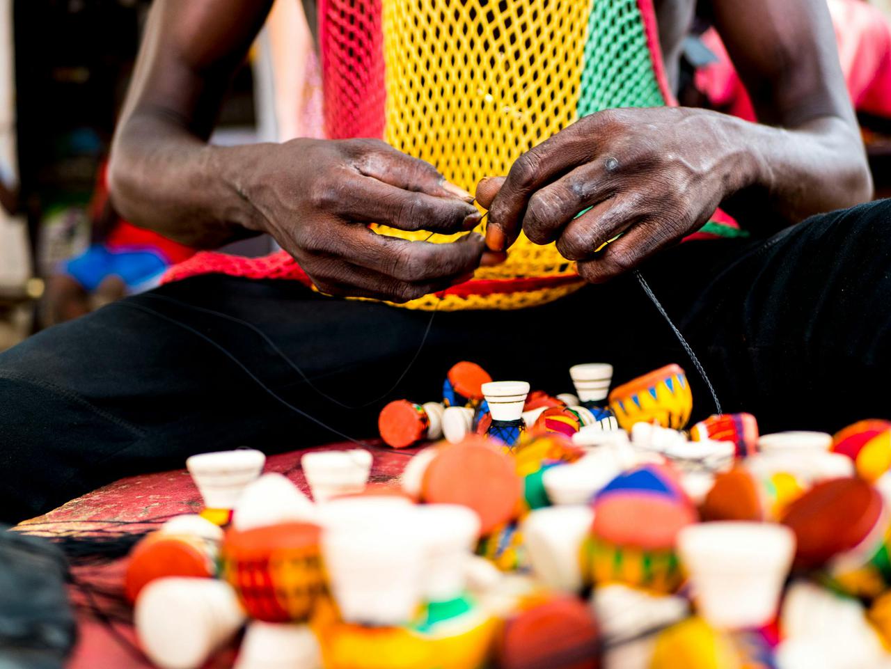 A close-up of an artisan in Ghana crafting vibrant miniature drums by hand, showcasing traditional African artistry.
