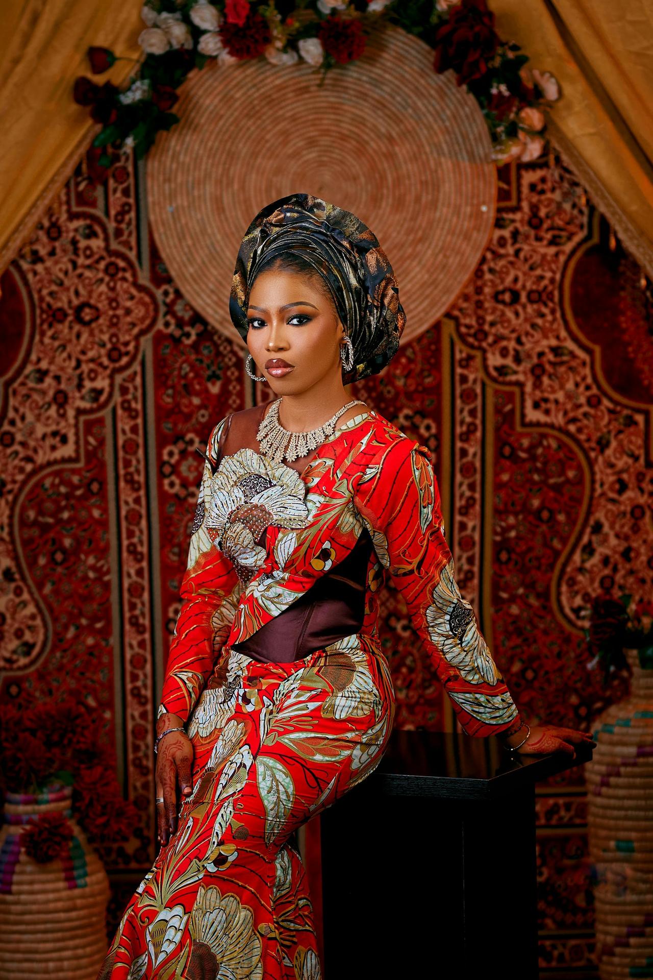 Portrait of a woman in vibrant traditional African clothing with decorative backdrop.