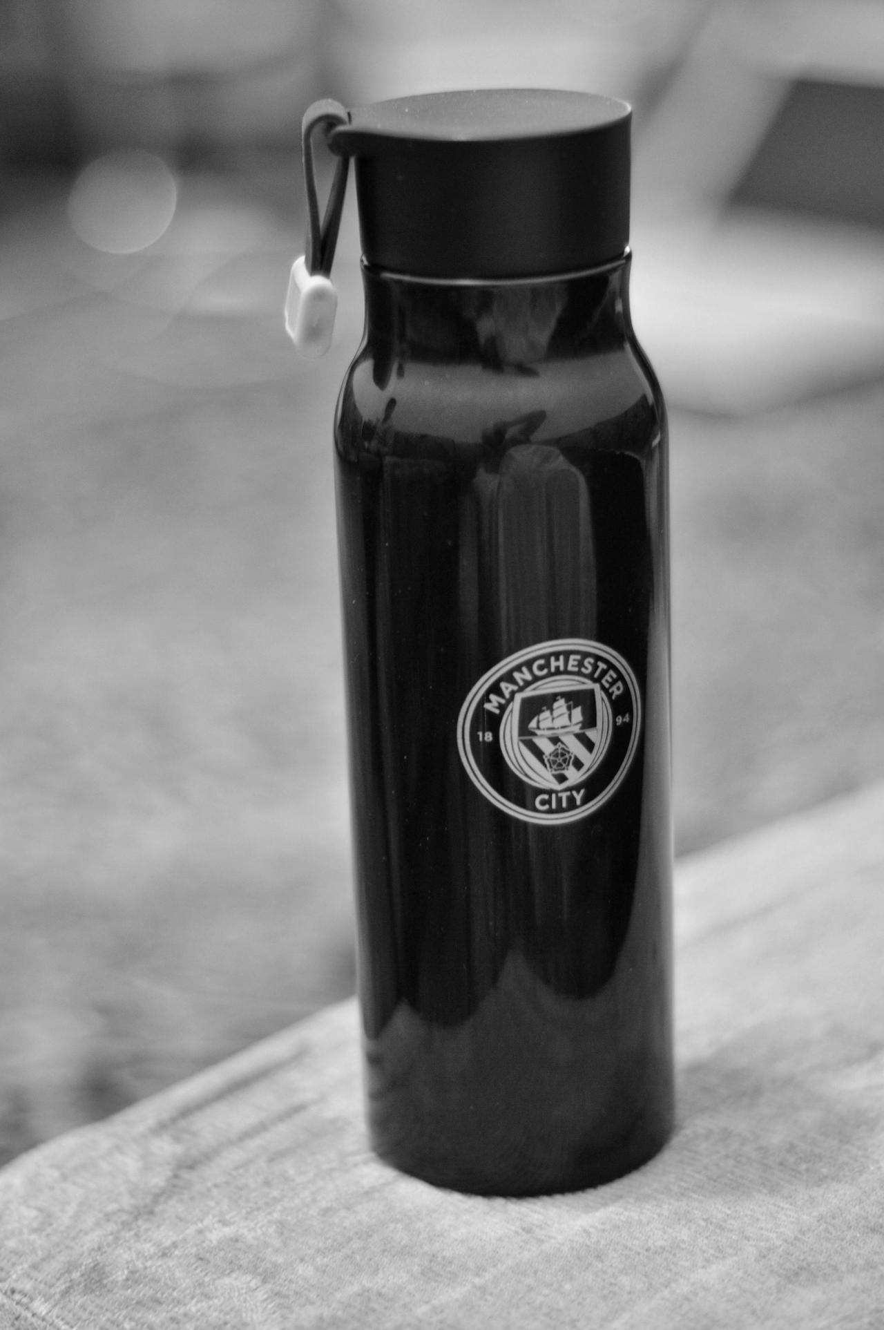 Black and white image of a Manchester City branded water bottle on a table.