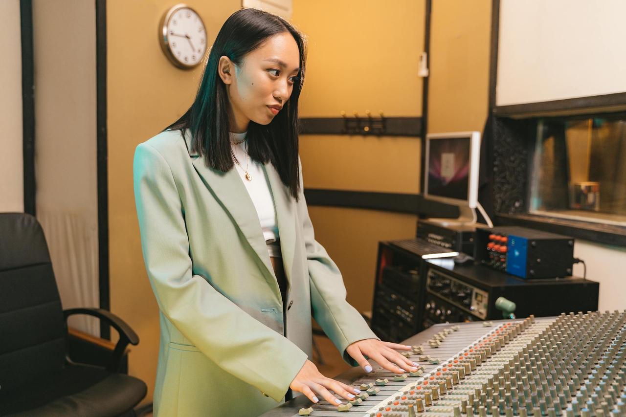 Asian woman in a blazer managing audio controls in a recording studio.