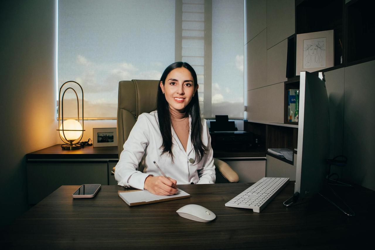 Confident woman working at desk in modern office with computer and paperwork.