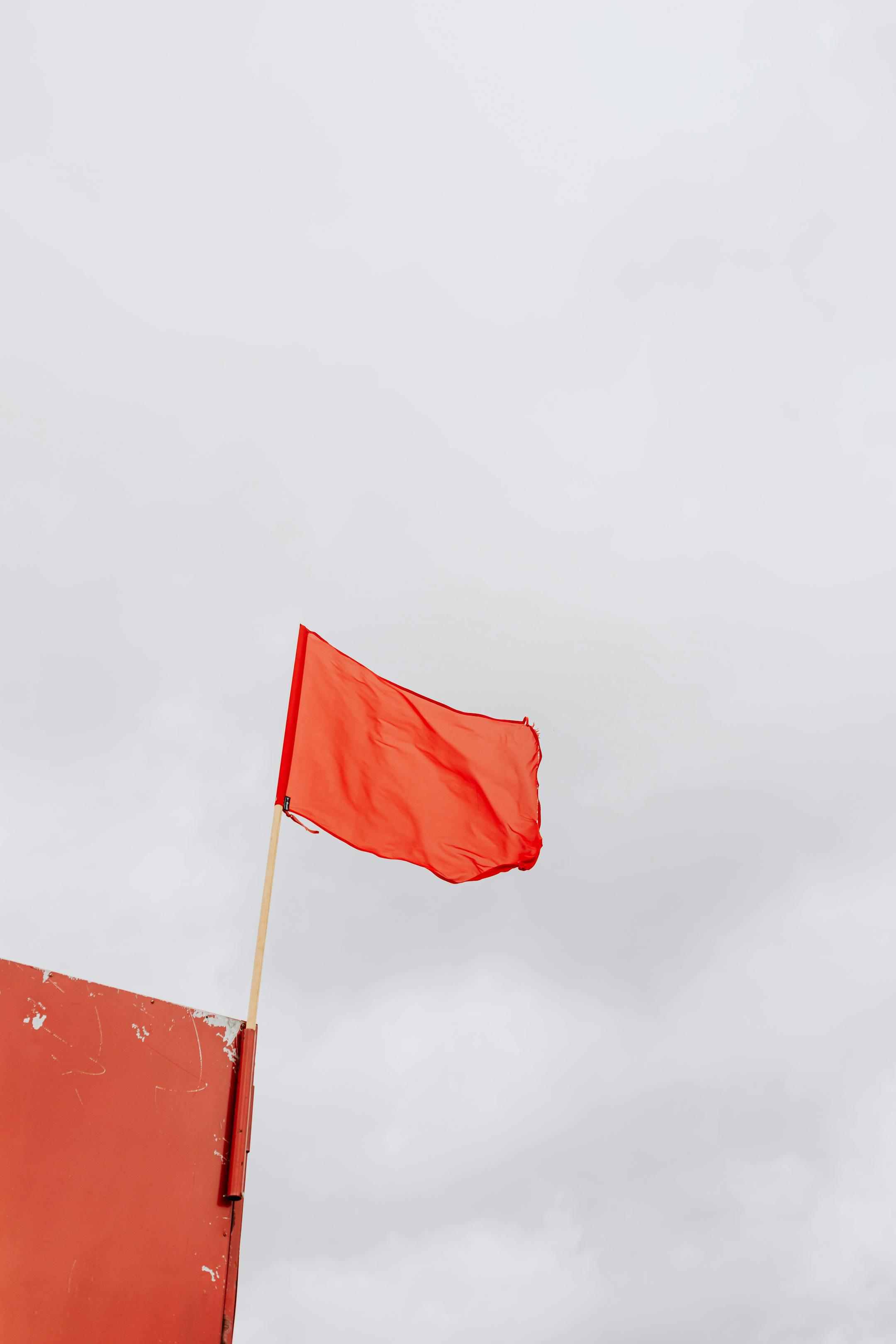 A red flag on a lifeguard tower set against a cloudy gray sky, symbolizing caution.
