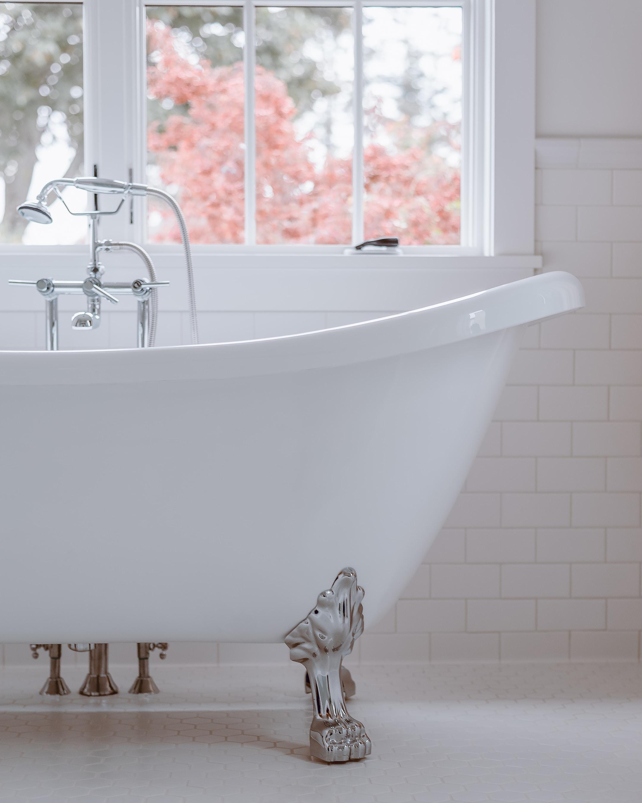 A white bathtub with flowers behind it outside the window.