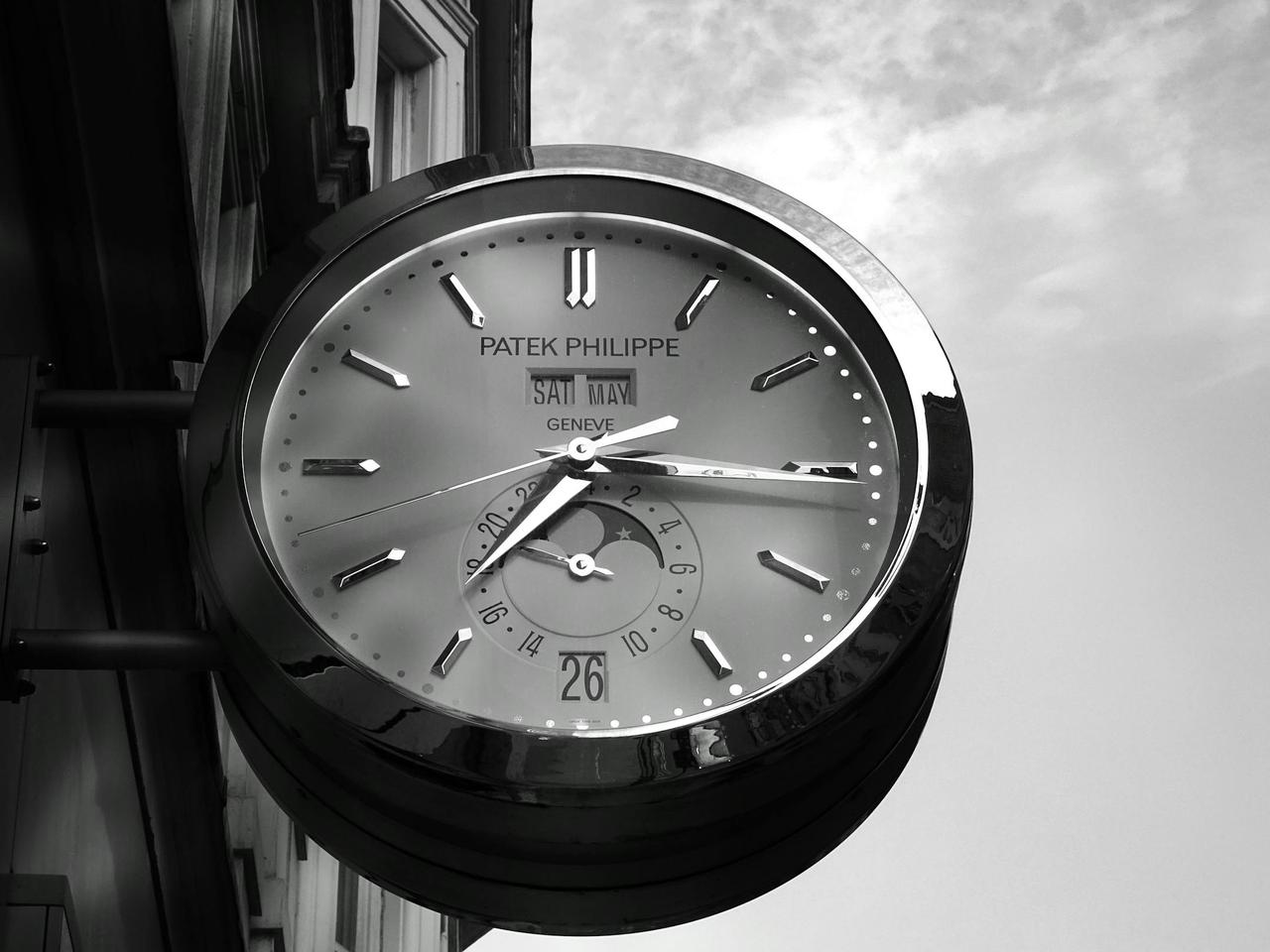 A close-up of a Patek Philippe wall clock with reflective surface showing time.