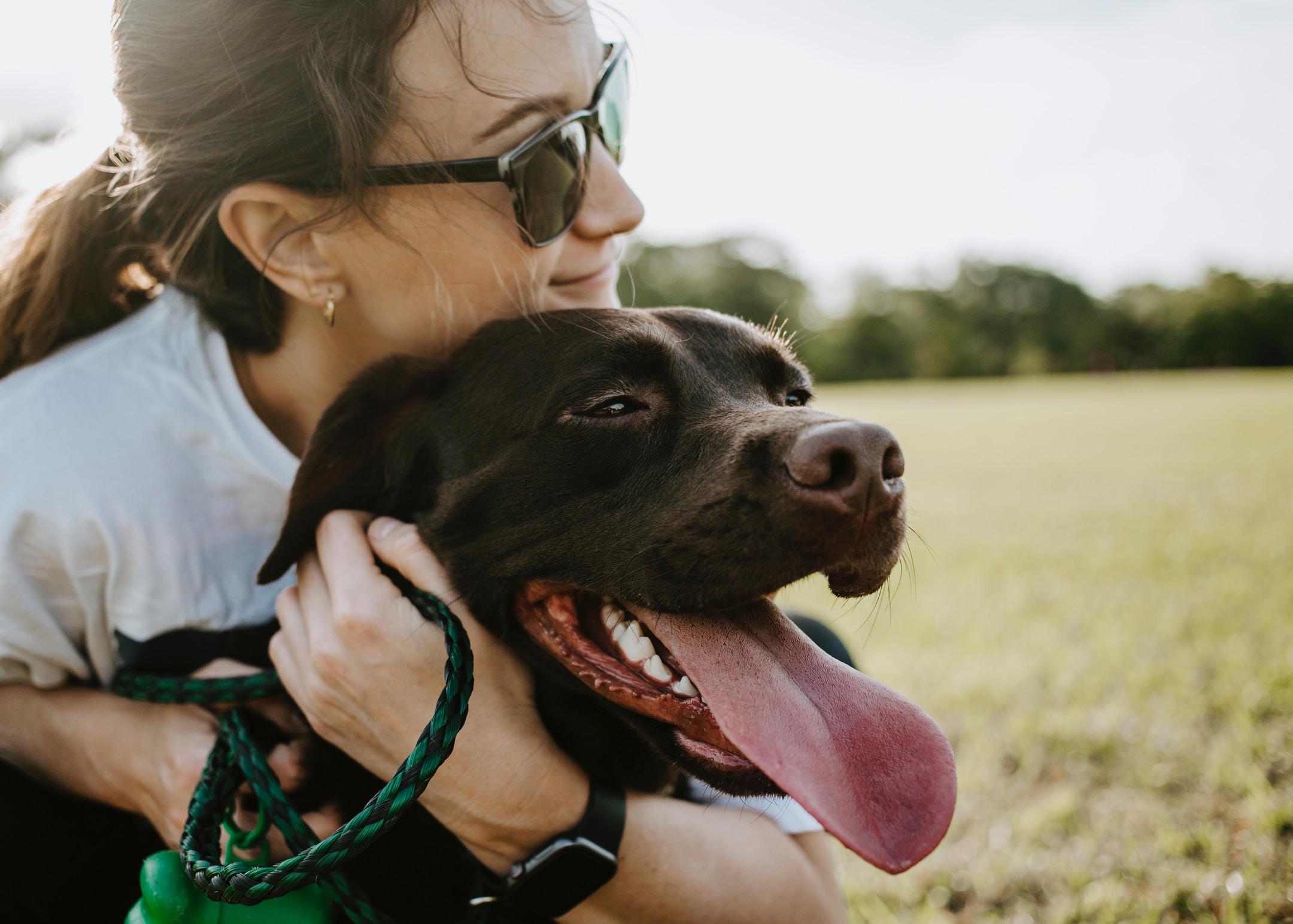 A girl with sunglasses hugging her dog in a field