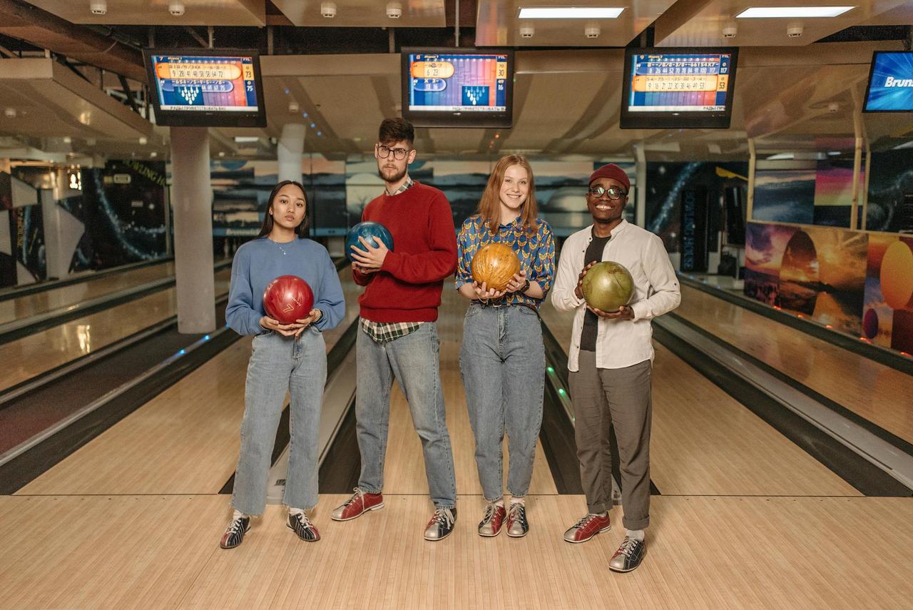 A diverse group of friends holding colorful bowling balls at an indoor alley.