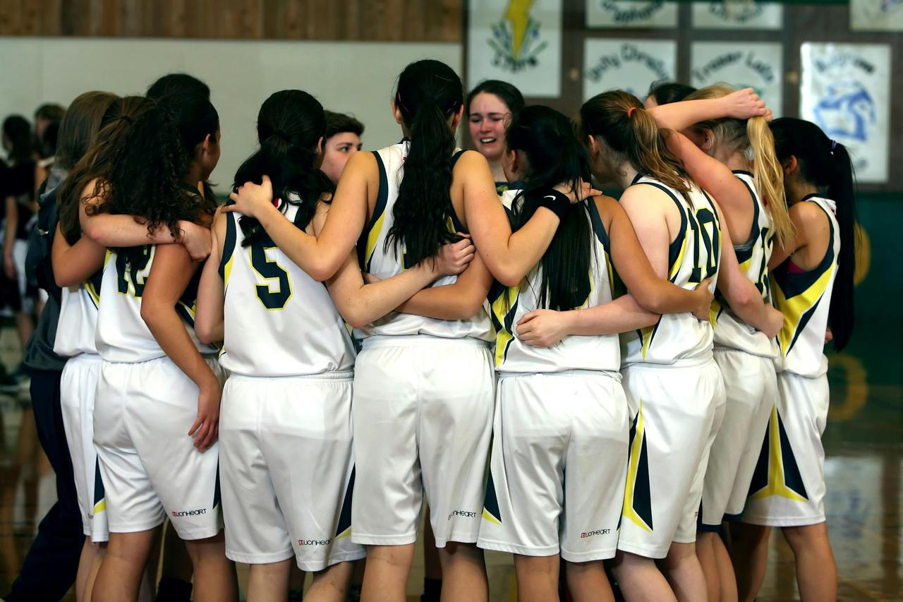 A girls' basketball team huddling before a game, showcasing teamwork and camaraderie.