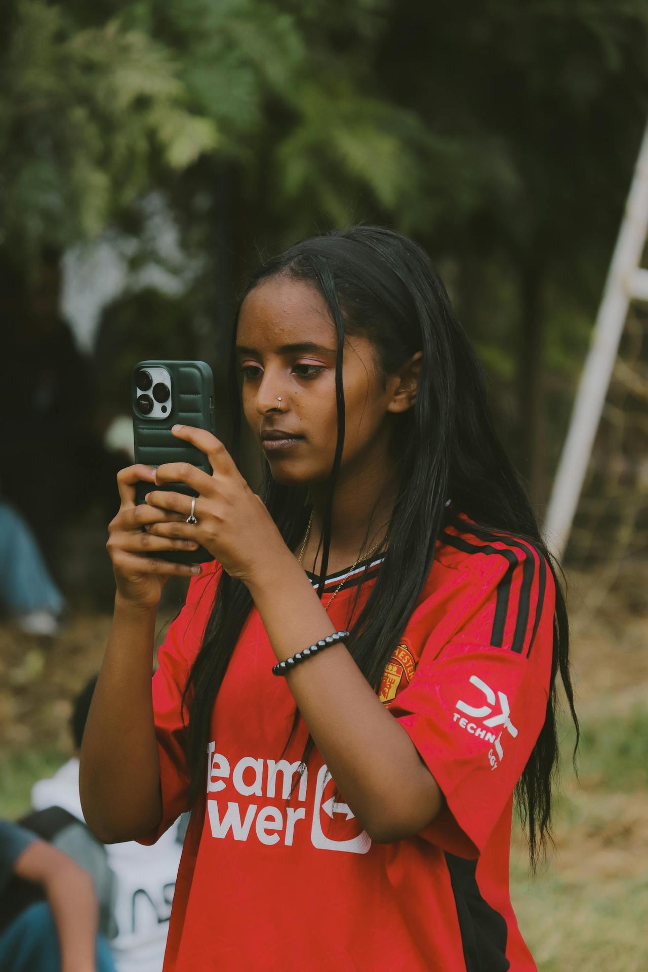 Teenage girl in Addis Ababa using smartphone while wearing a football jersey.