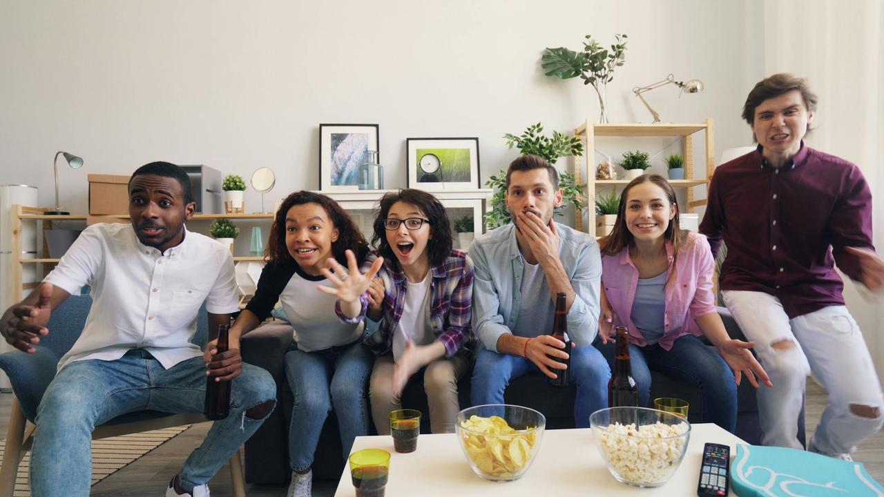 A diverse group of friends enjoying a sports game together indoors with snacks.