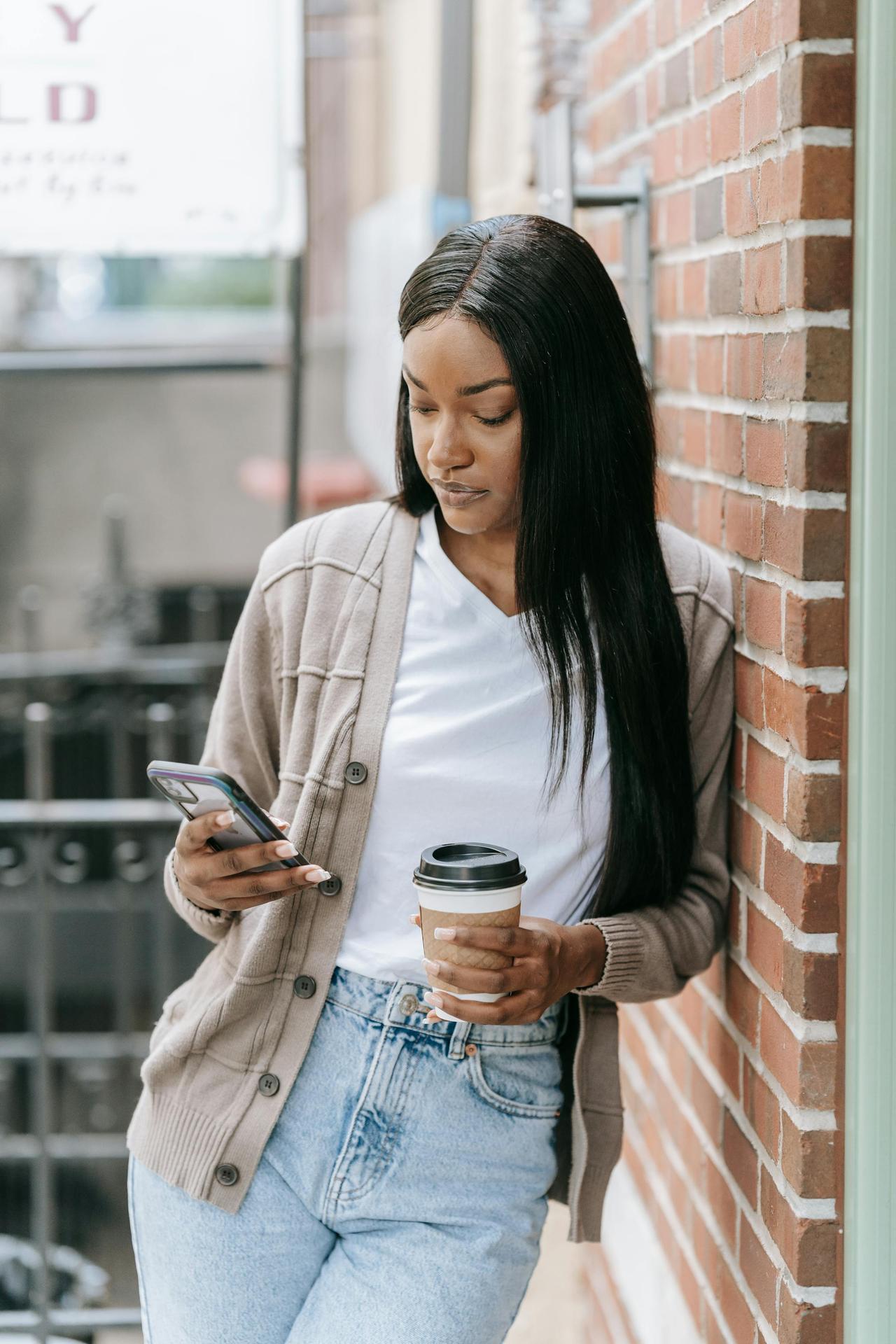 Casual young woman with coffee cup checking her phone outdoors on a relaxed day.