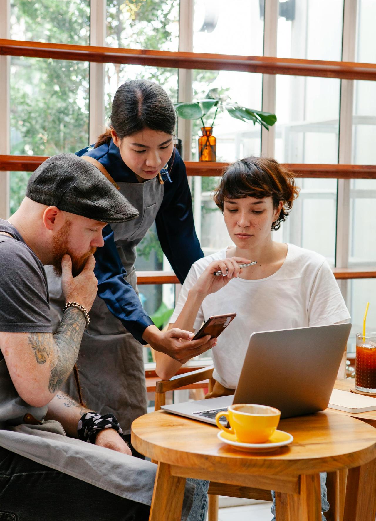 Diverse group of adults discussing ideas with a laptop and smartphone in a café setting.
