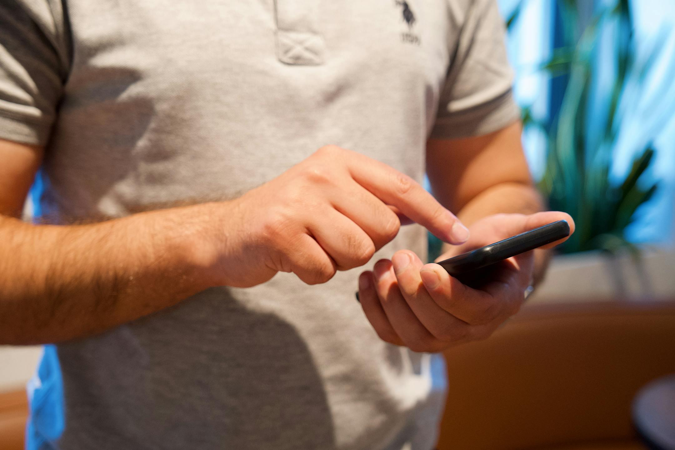 Adult male using smartphone in a bright indoor setting, focusing on the device and interaction.