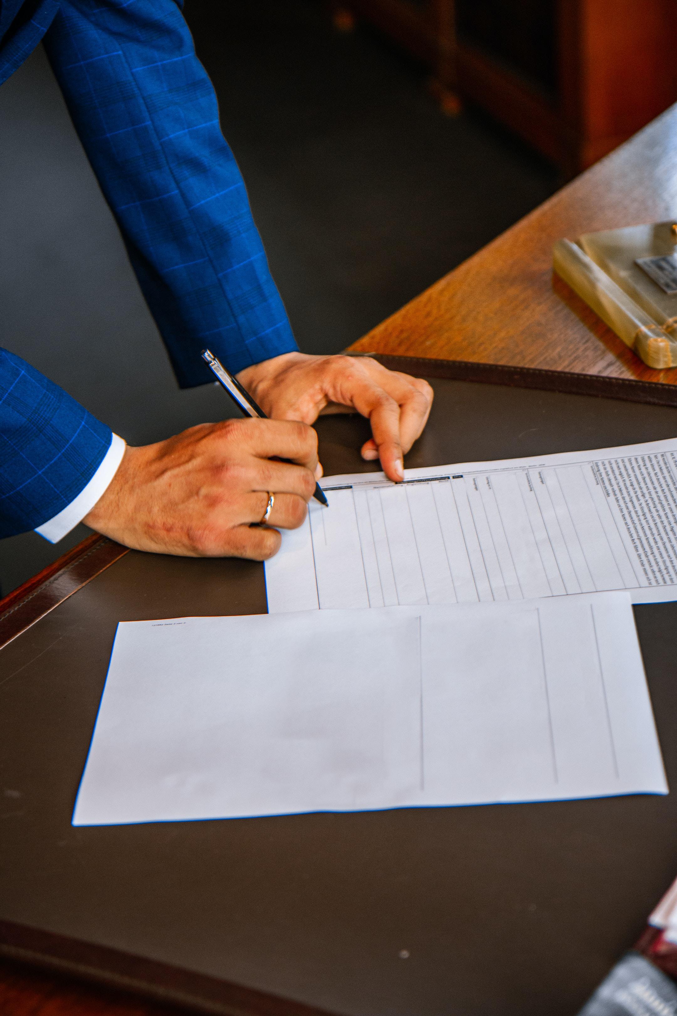 Hands resting on a desk and jotting on documents.