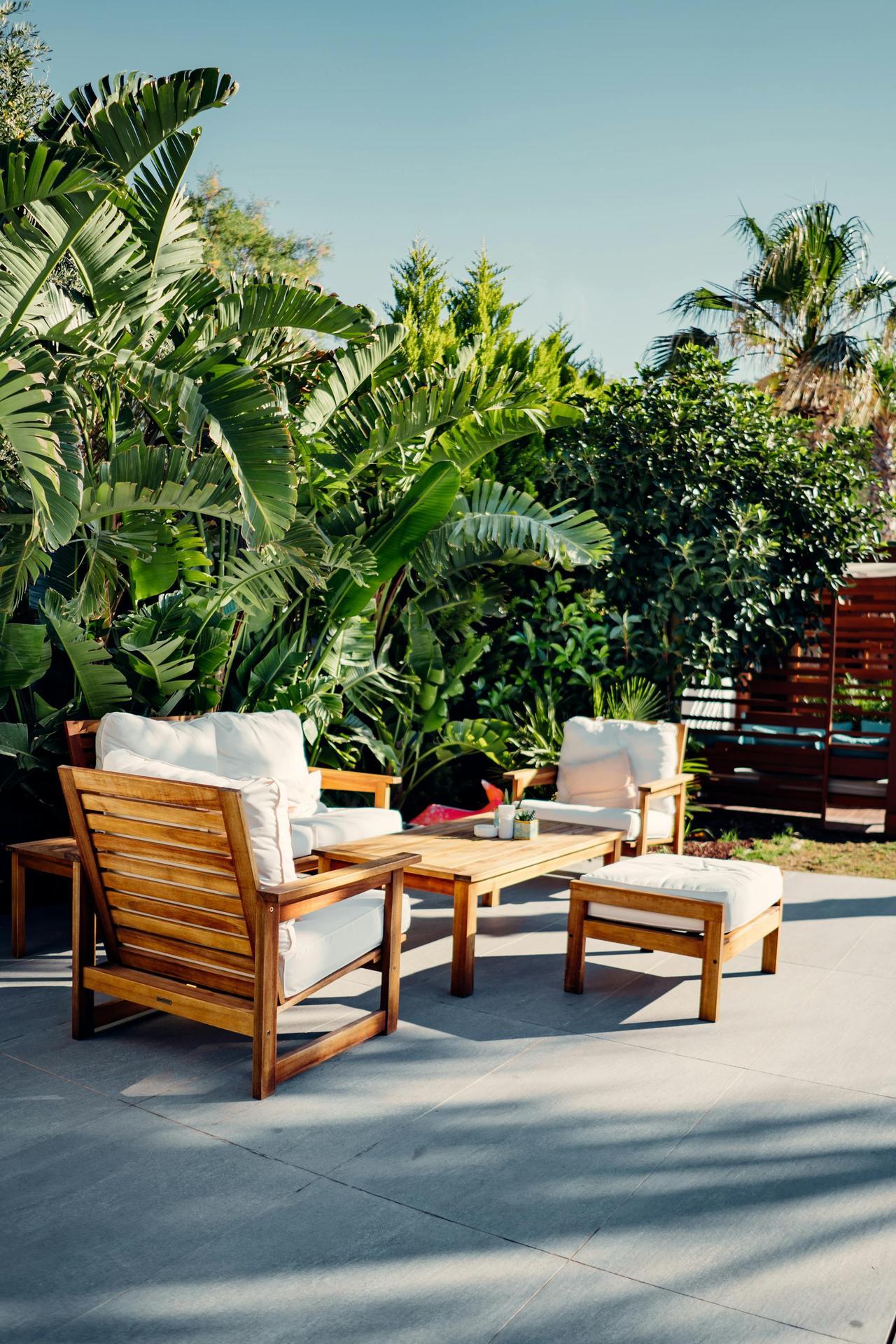 Elegant outdoor patio featuring wooden chairs and lush tropical plants under a clear sky.